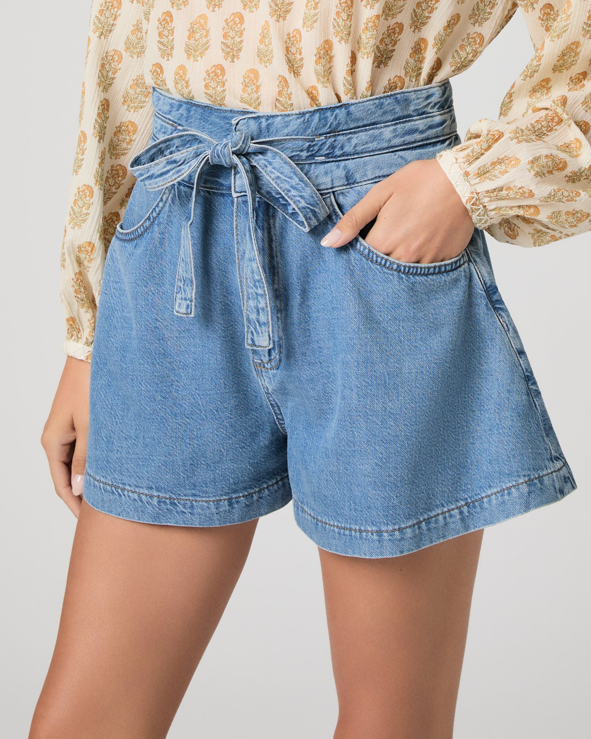 Woman wearing a patterned blouse and denim shorts on a white background