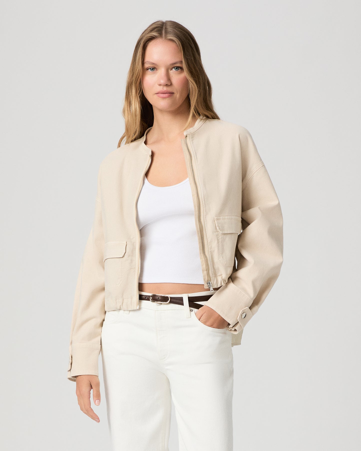 Woman wearing a beige jacket over a white top and pants on a light gray background