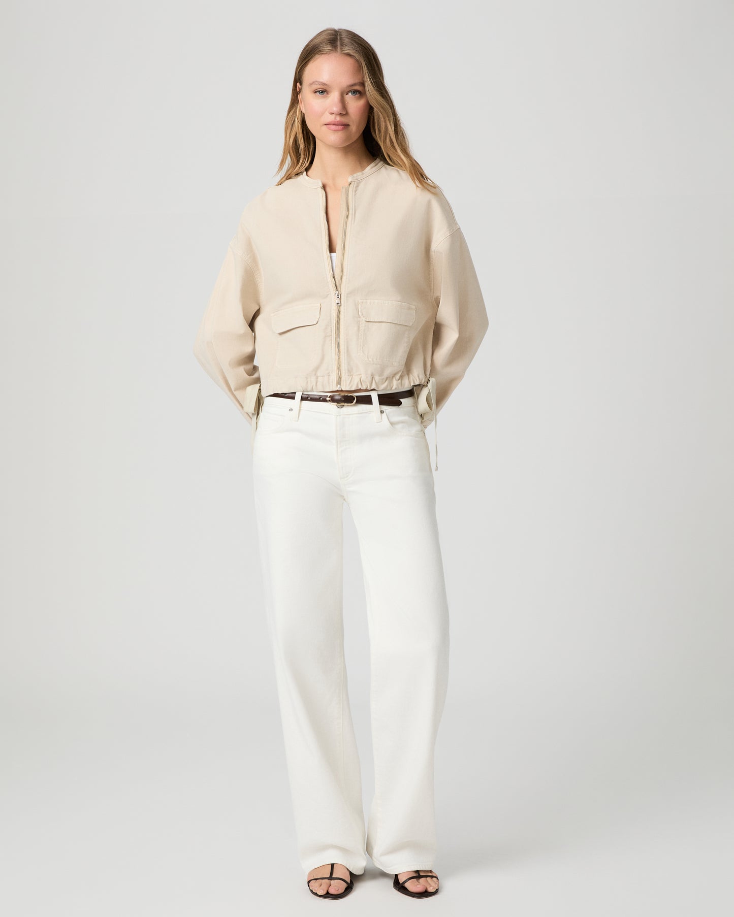 Woman wearing a beige jacket over a white top and pants on a light gray background