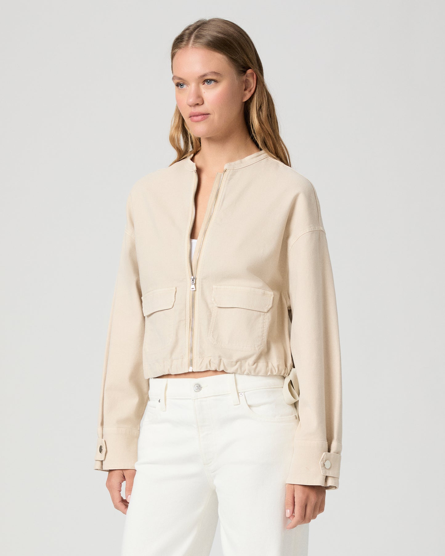 Woman wearing a beige jacket over a white top and pants on a light gray background