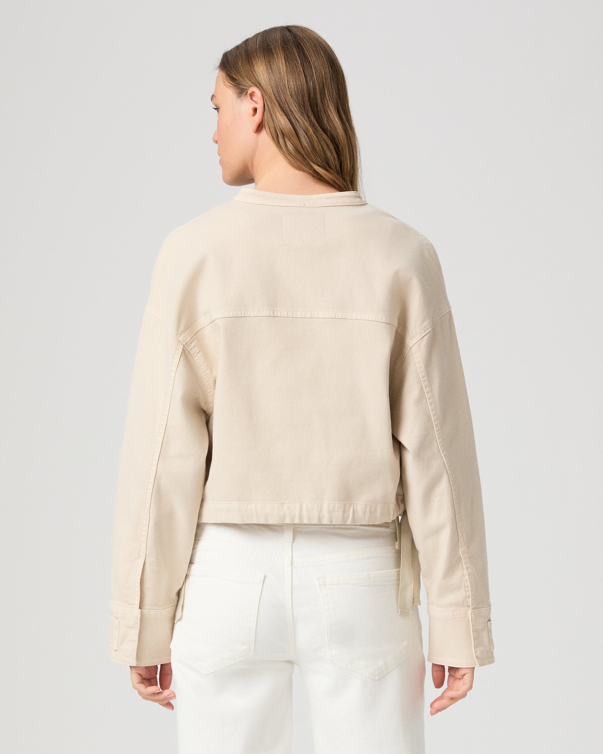 Woman wearing a beige jacket over a white top and pants on a light gray background