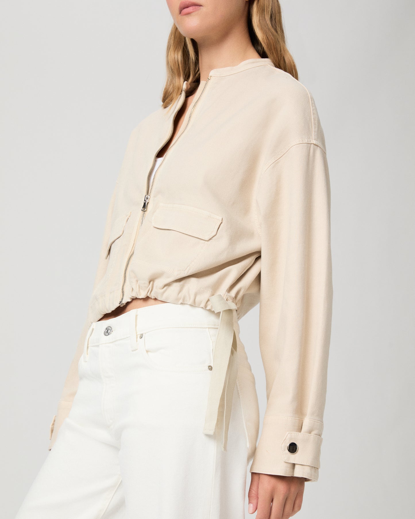 Woman wearing a beige jacket over a white top and pants on a light gray background