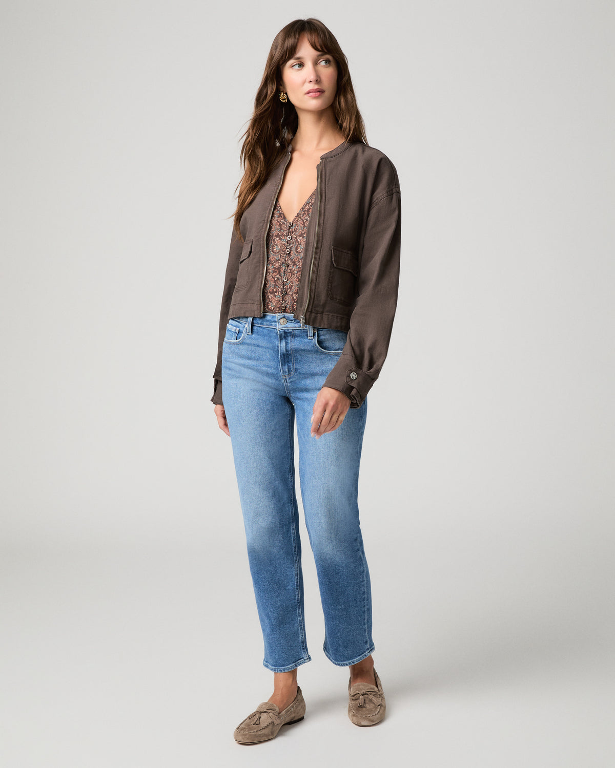 Woman wearing brown jacket and blue pants with a white background.