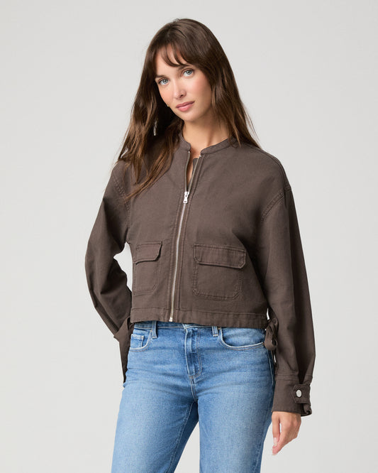 Woman wearing brown jacket and blue pants with a white background.