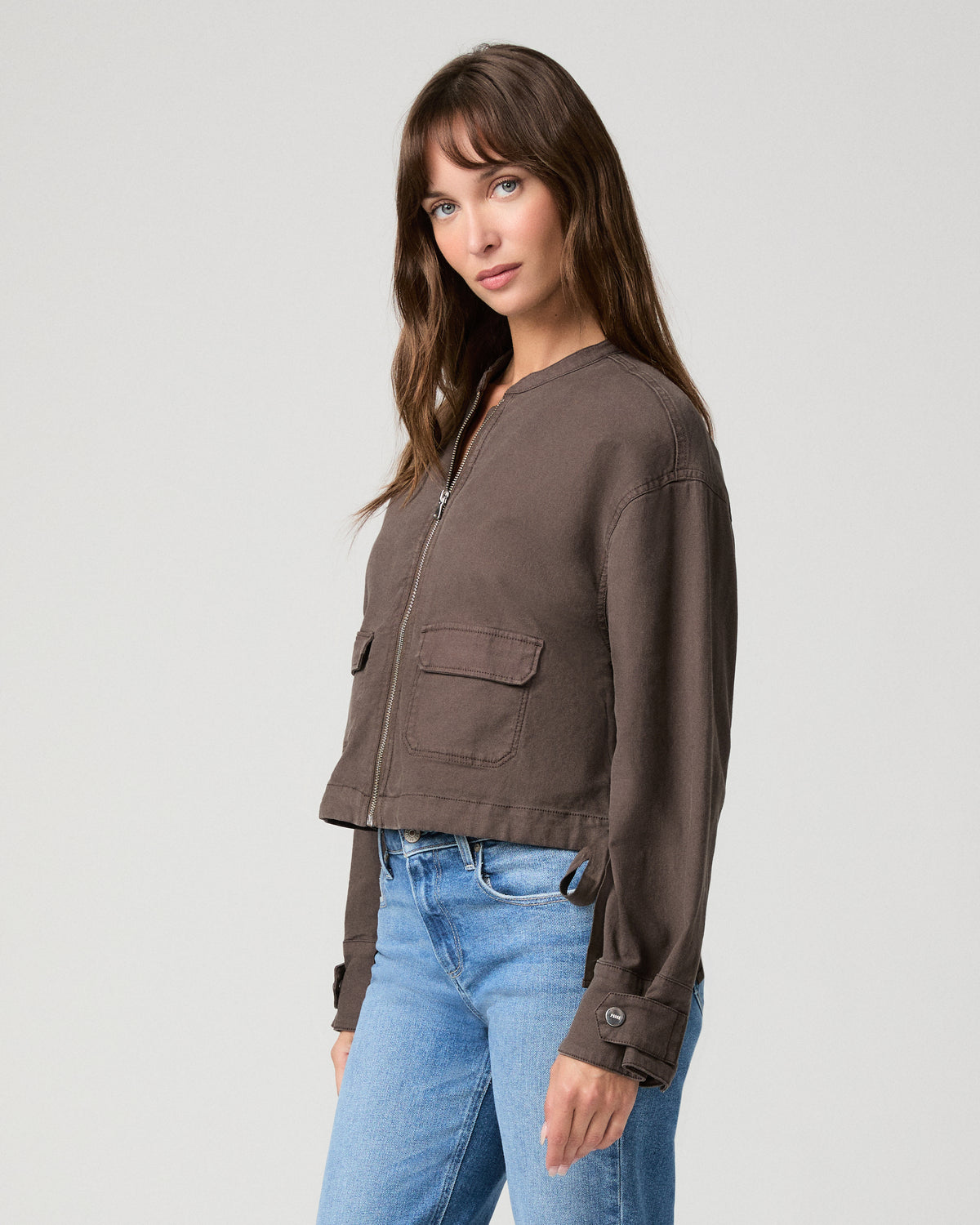 Woman wearing brown jacket and blue pants with a white background.