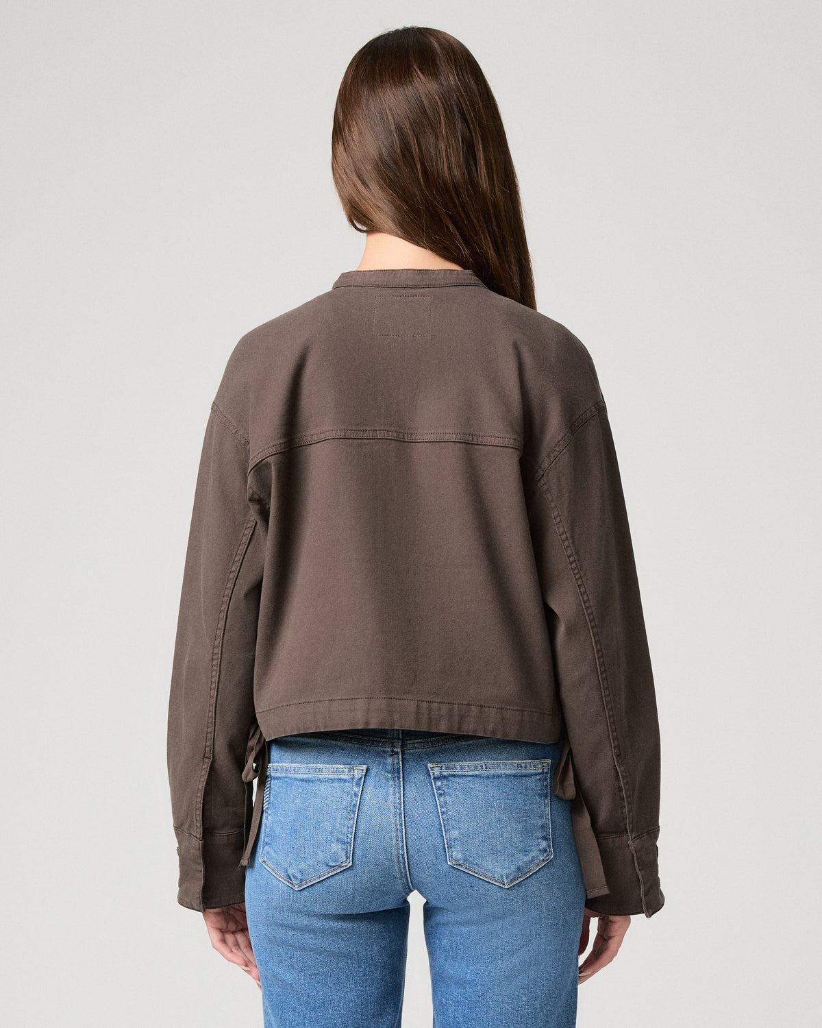 Woman wearing brown jacket and blue pants with a white background.