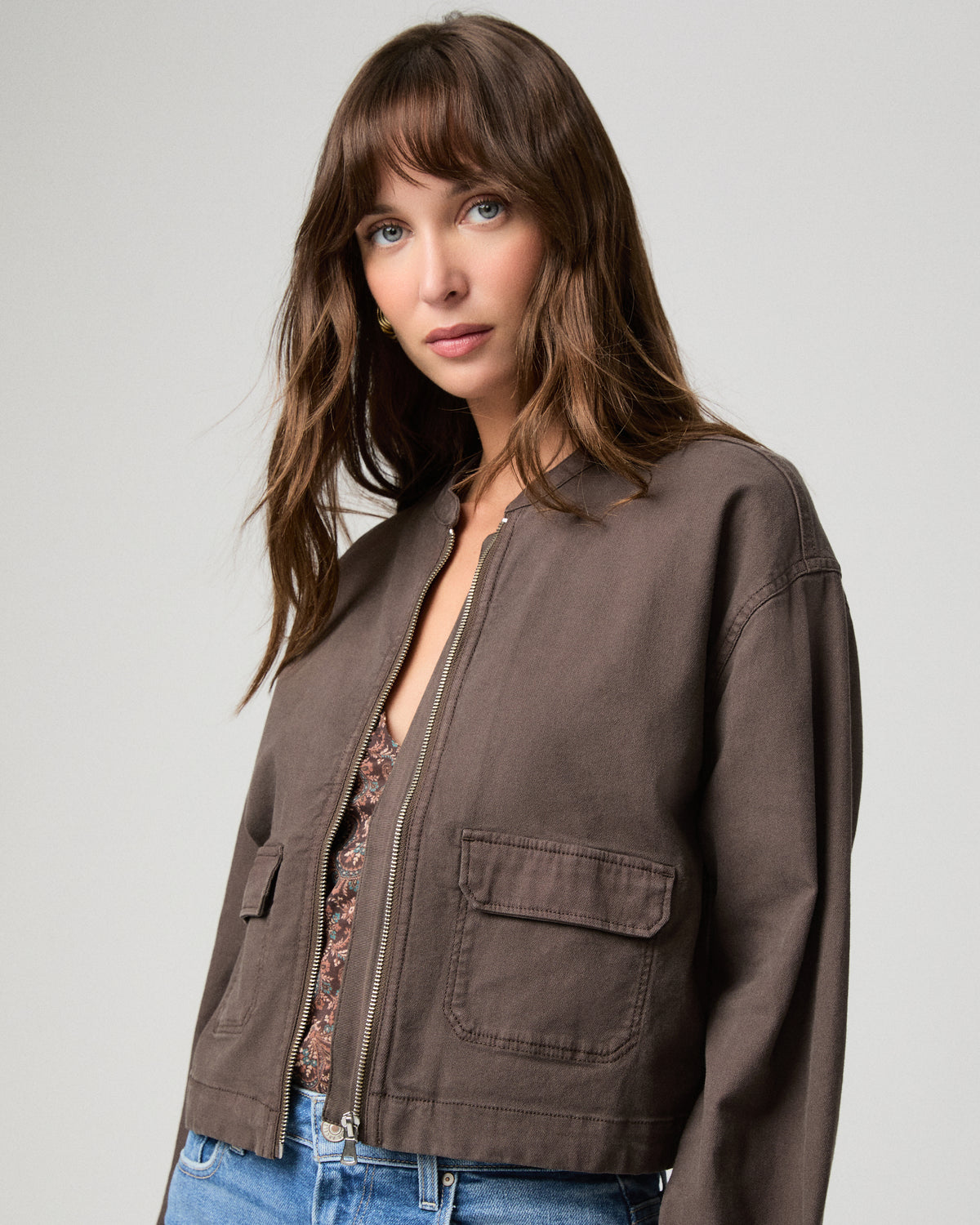 Woman wearing brown jacket and blue pants with a white background.