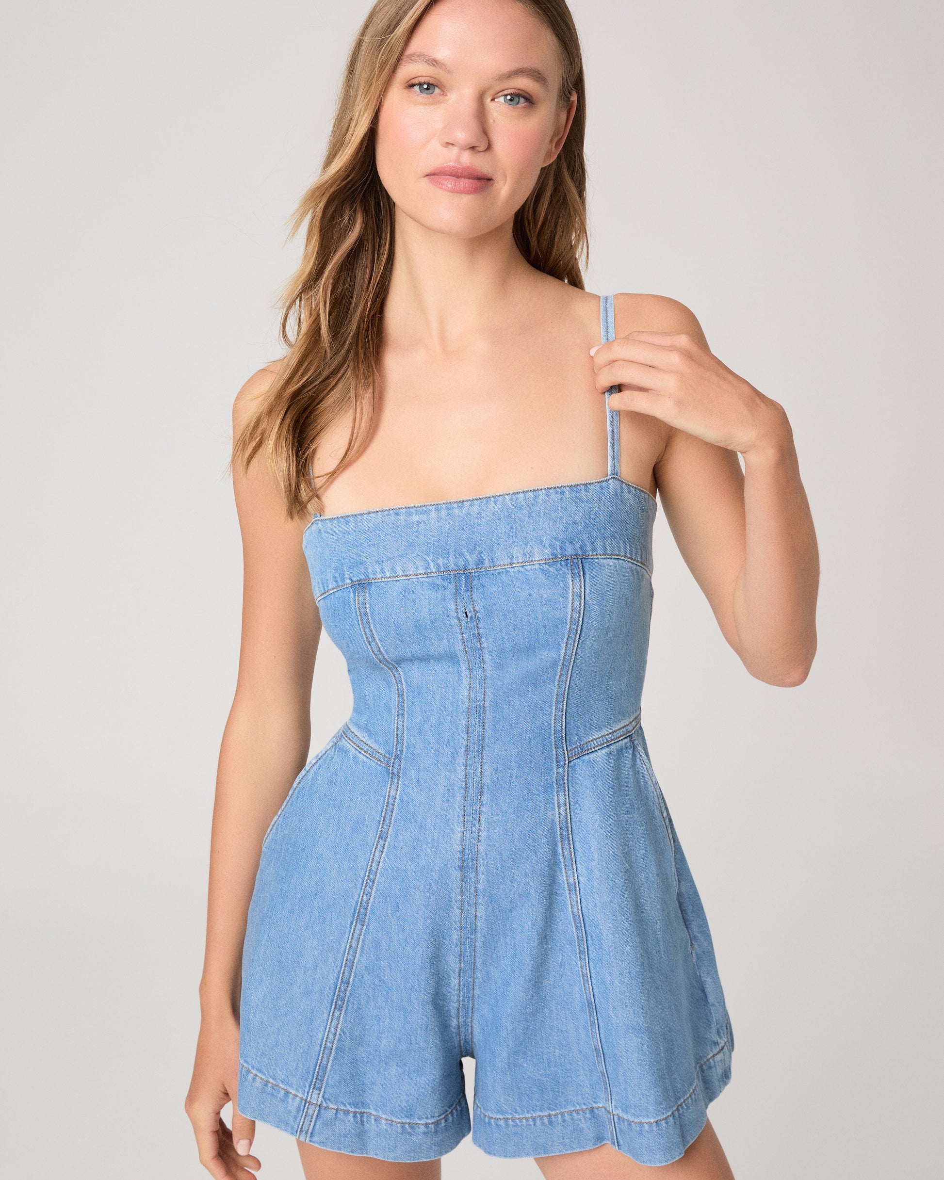 Woman wearing a denim romper paired with brown wedges on a white background