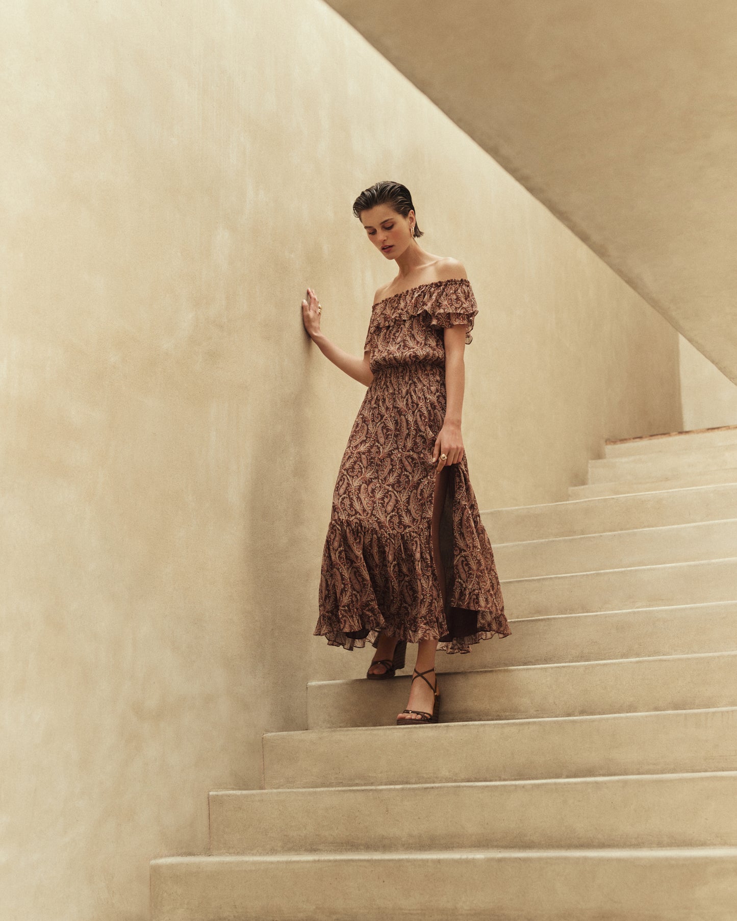 Woman in a patterned brown dress standing on a staircase with a neutral wall background