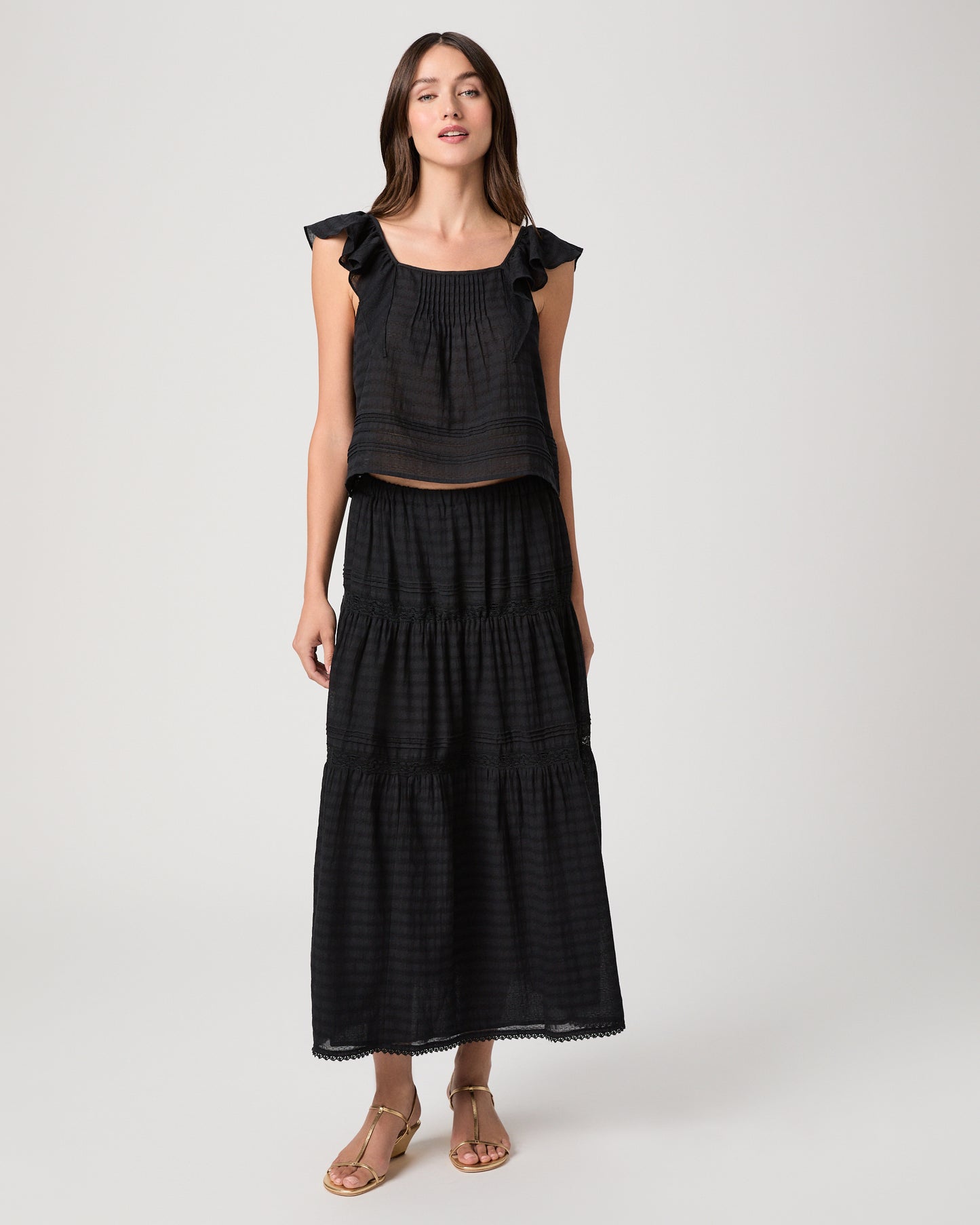 Model wearing a black midi skirt paired with a black  top and gold sandals