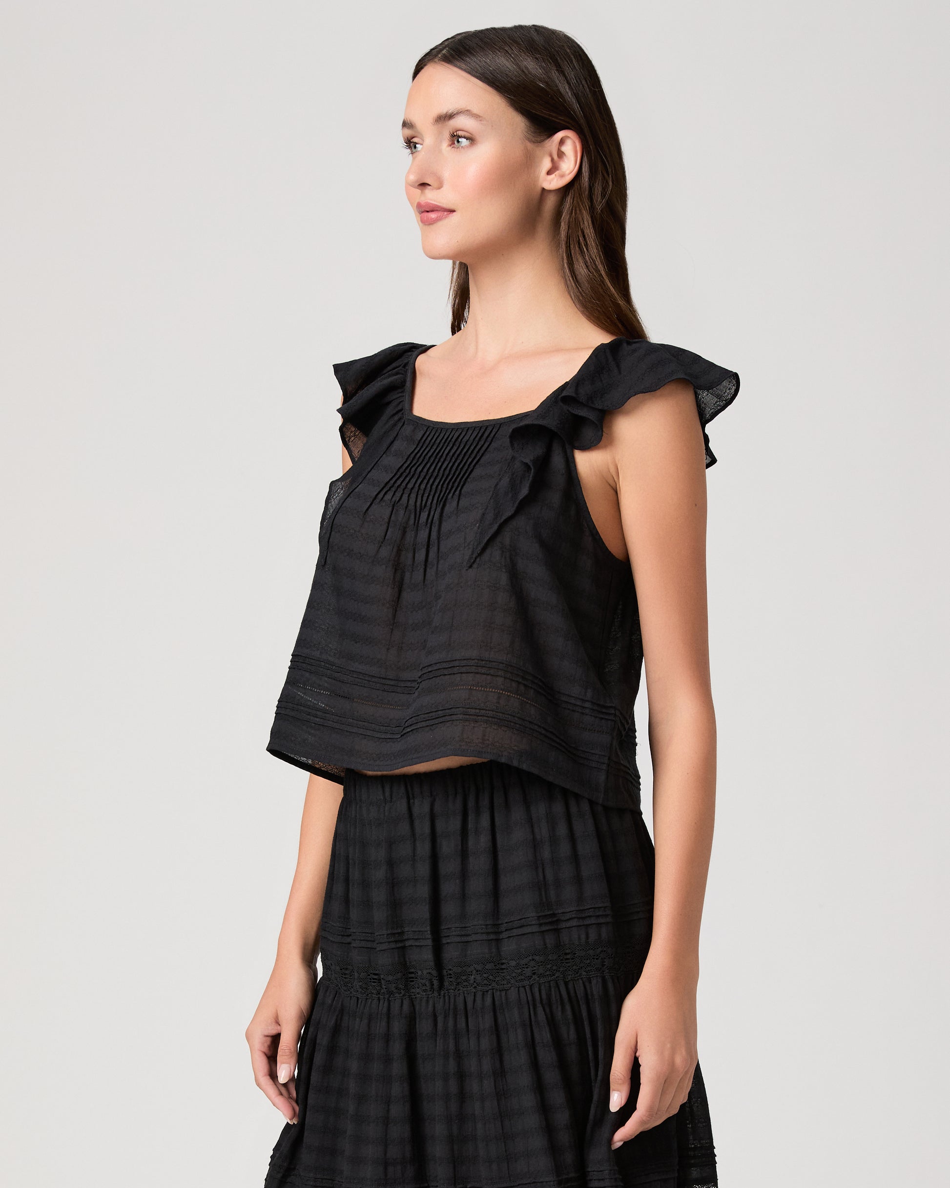Model wearing a black midi skirt paired with a black  top and gold sandals