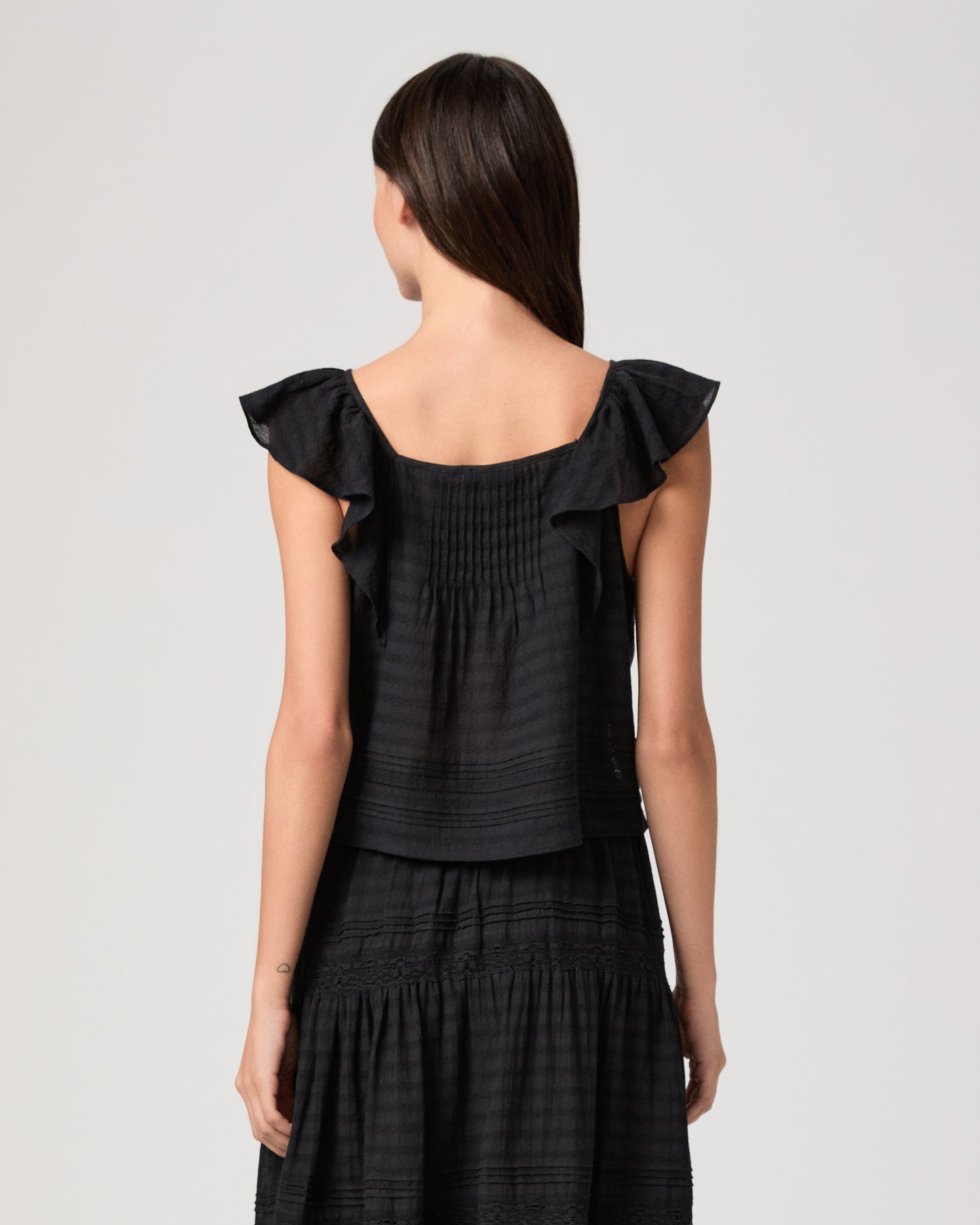 Model wearing a black midi skirt paired with a black  top and gold sandals