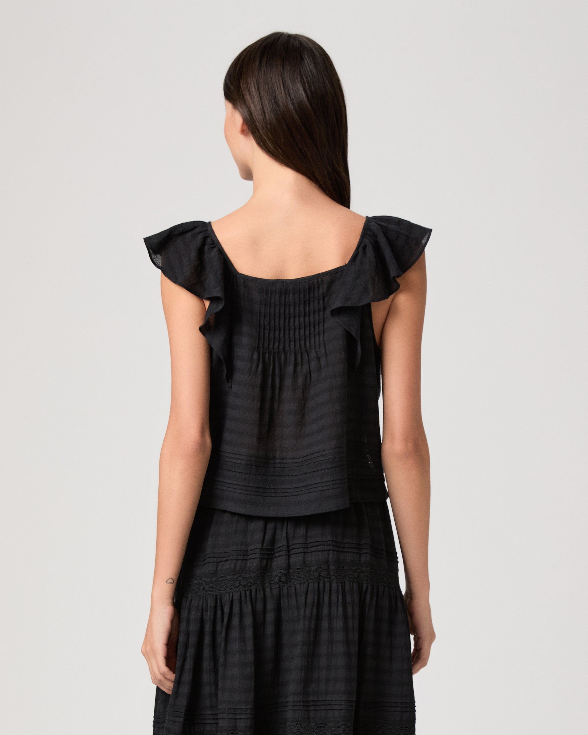 Model wearing a black midi skirt paired with a black  top and gold sandals