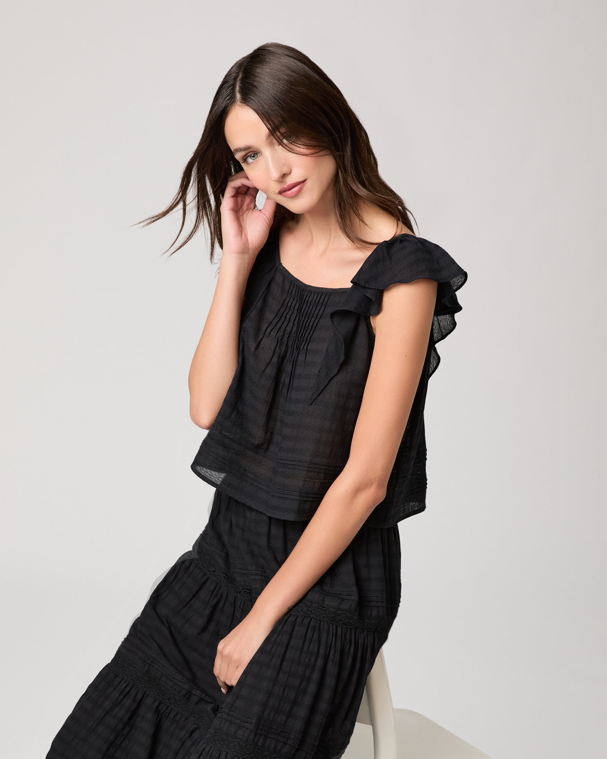 Model wearing a black midi skirt paired with a black  top and gold sandals