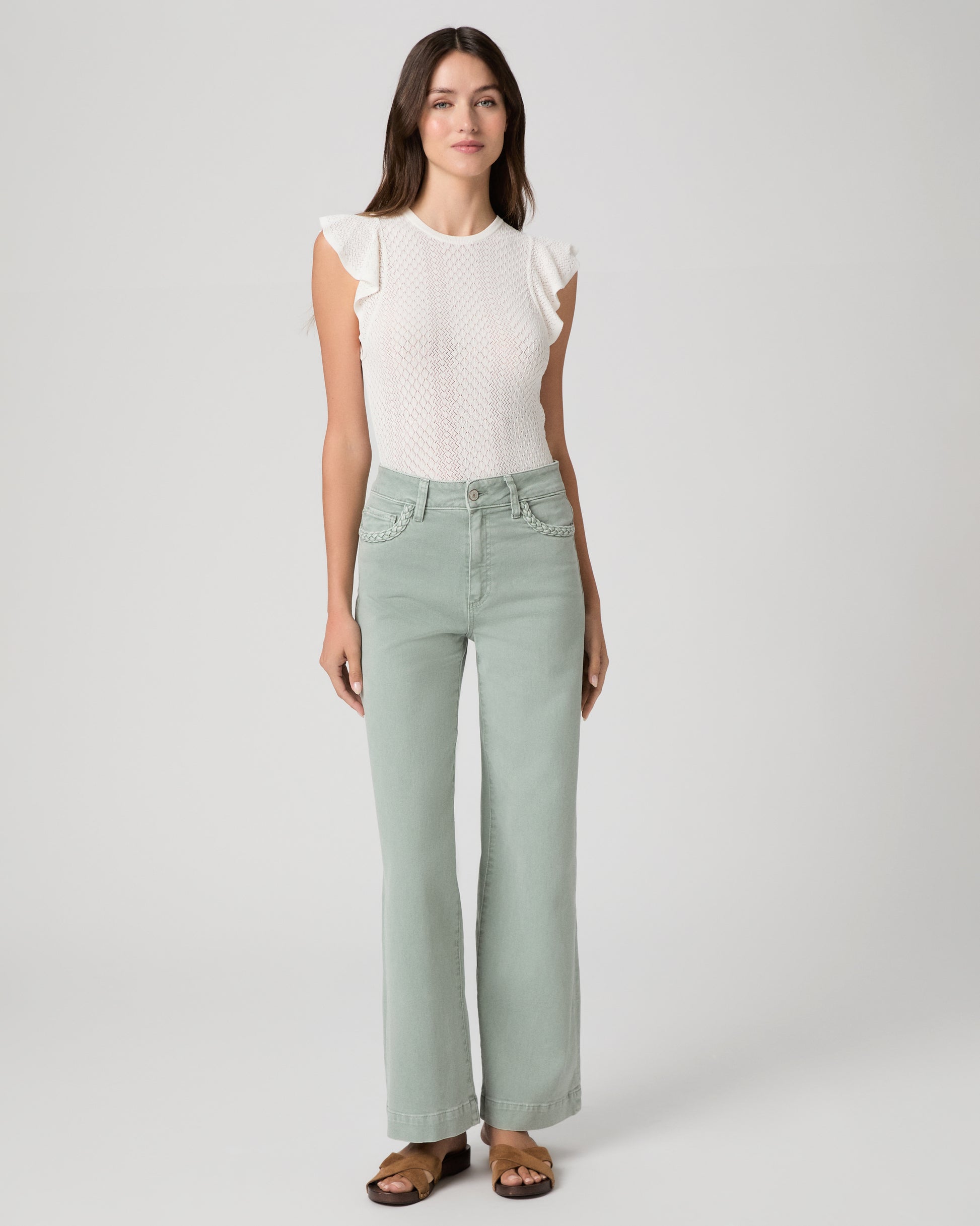 Woman wearing a white textured top and light green pants on a gray background