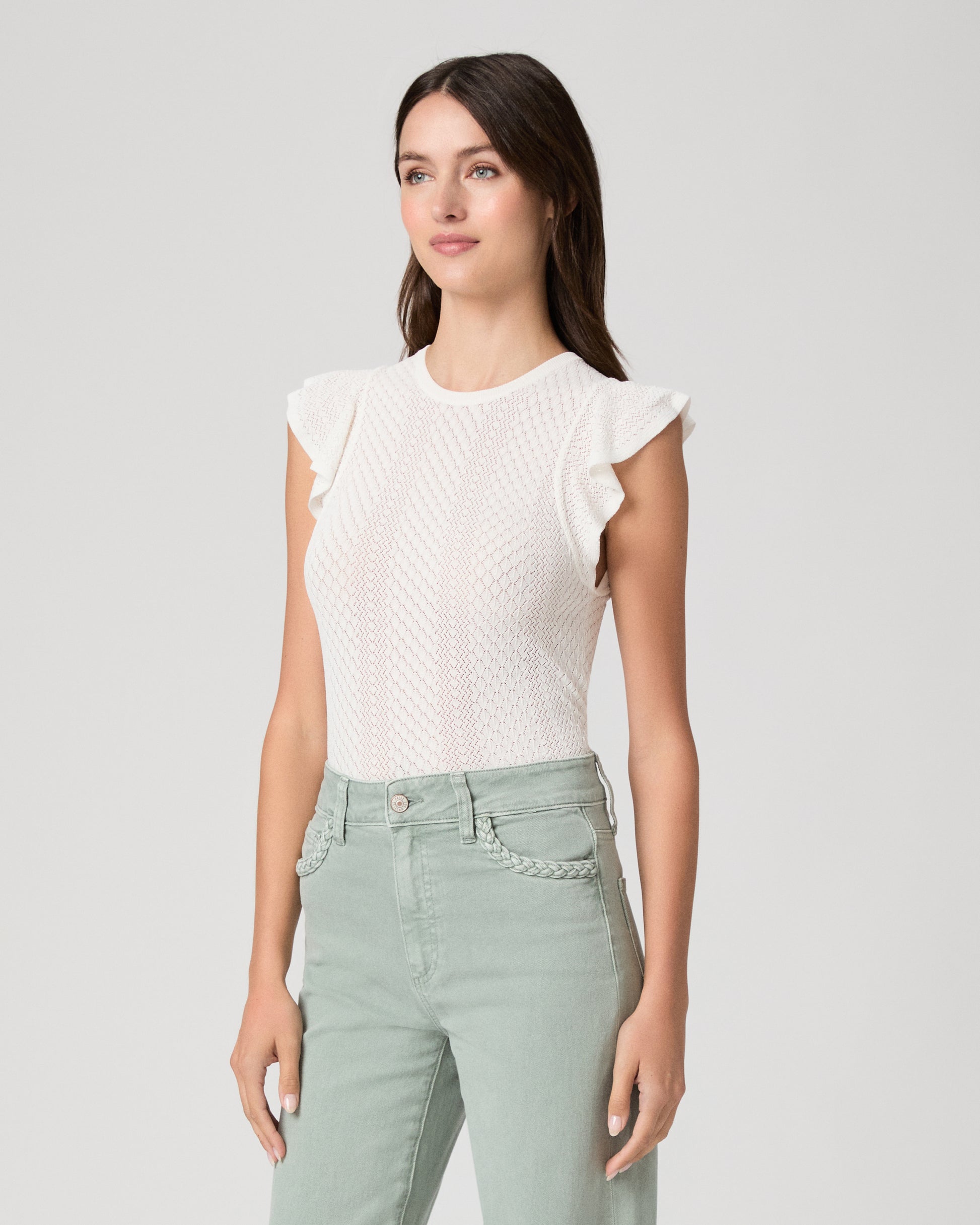 Woman wearing a white textured top and light green pants on a gray background