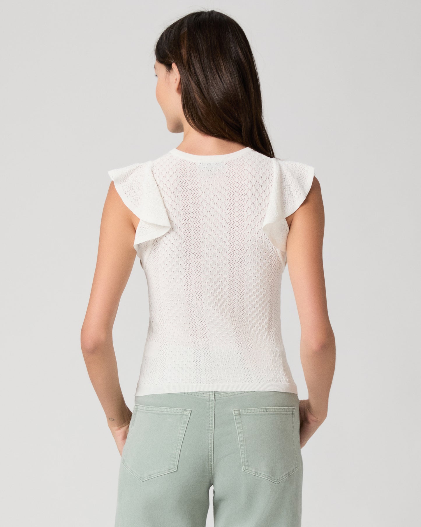 Woman wearing a white textured top and light green pants on a gray background