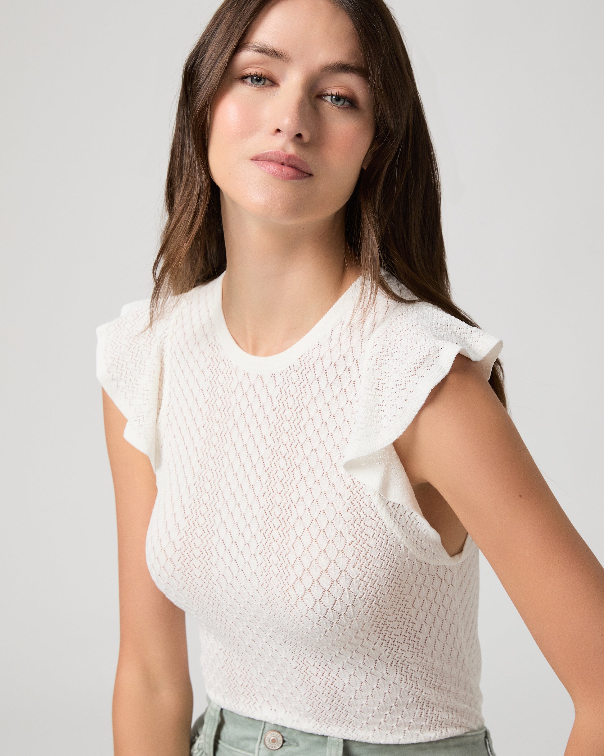 Woman wearing a white textured top and light green pants on a gray background