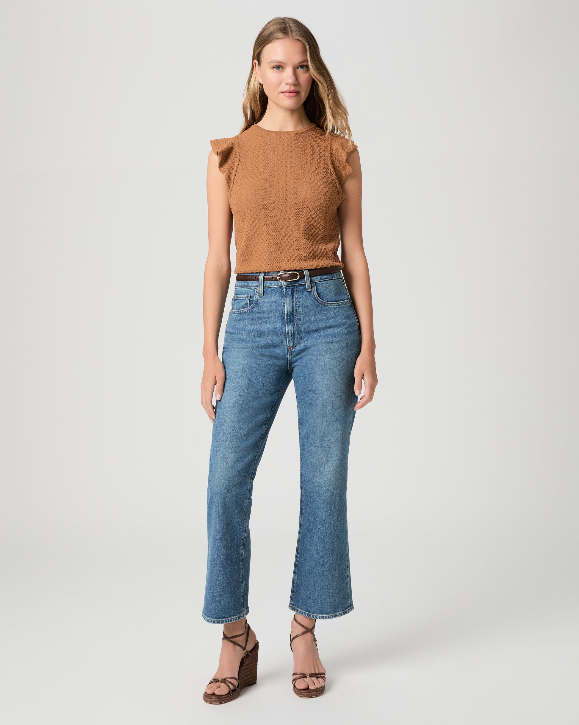 Woman wearing a brown textured top and blue jeans on a light gray background