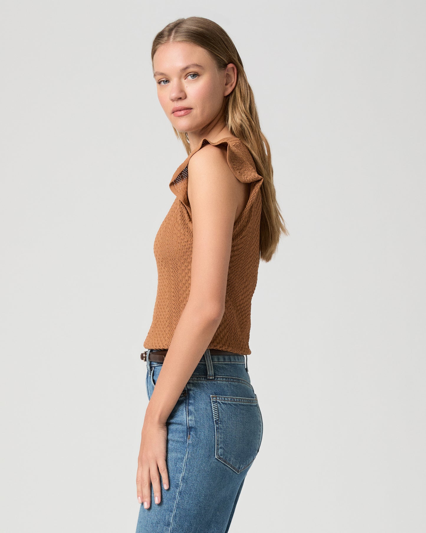Woman wearing a brown textured top and blue jeans on a light gray background