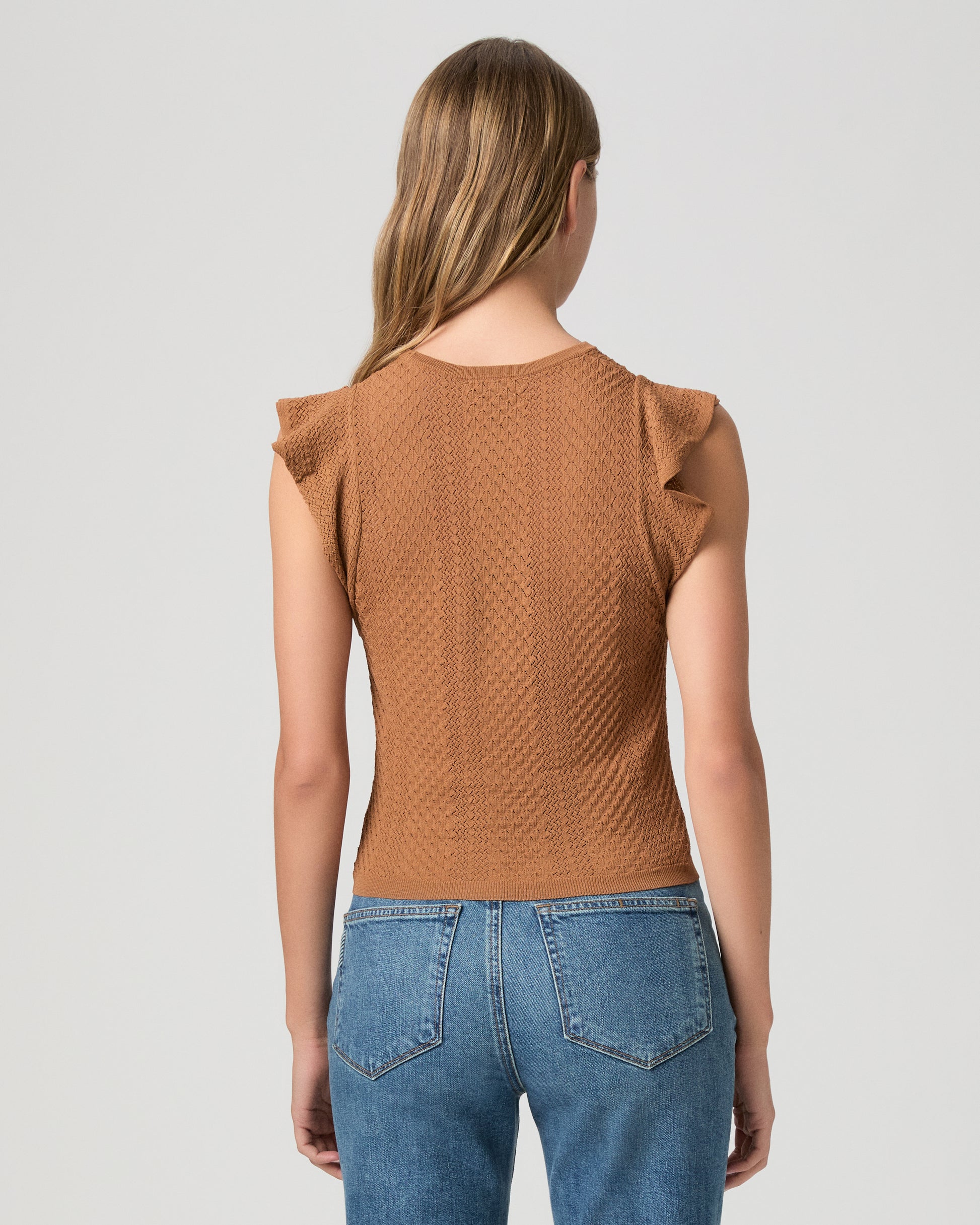 Woman wearing a brown textured top and blue jeans on a light gray background