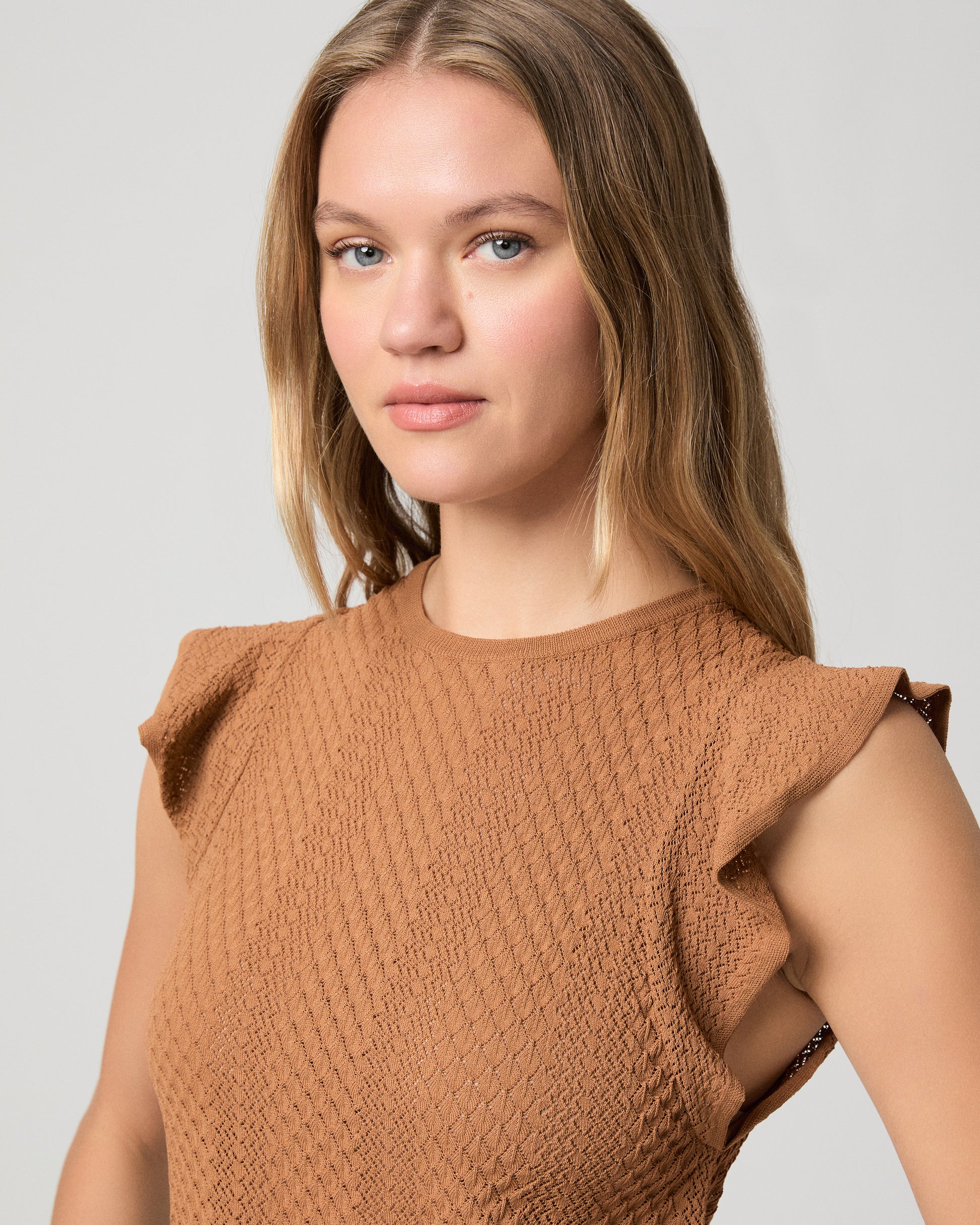 Woman wearing a brown textured top and blue jeans on a light gray background