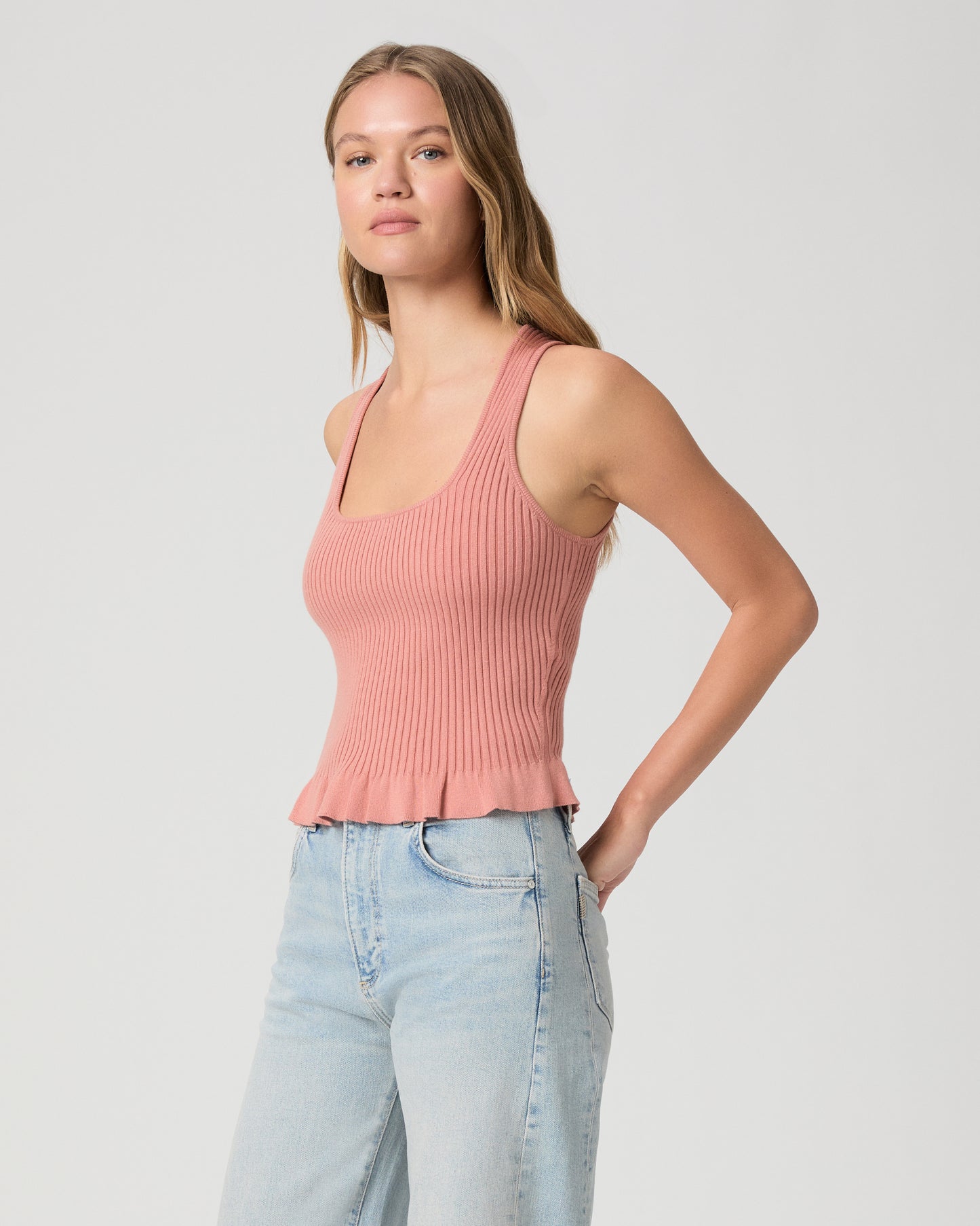 Woman wearing a pink ribbed tank top and light blue jeans on a plain background