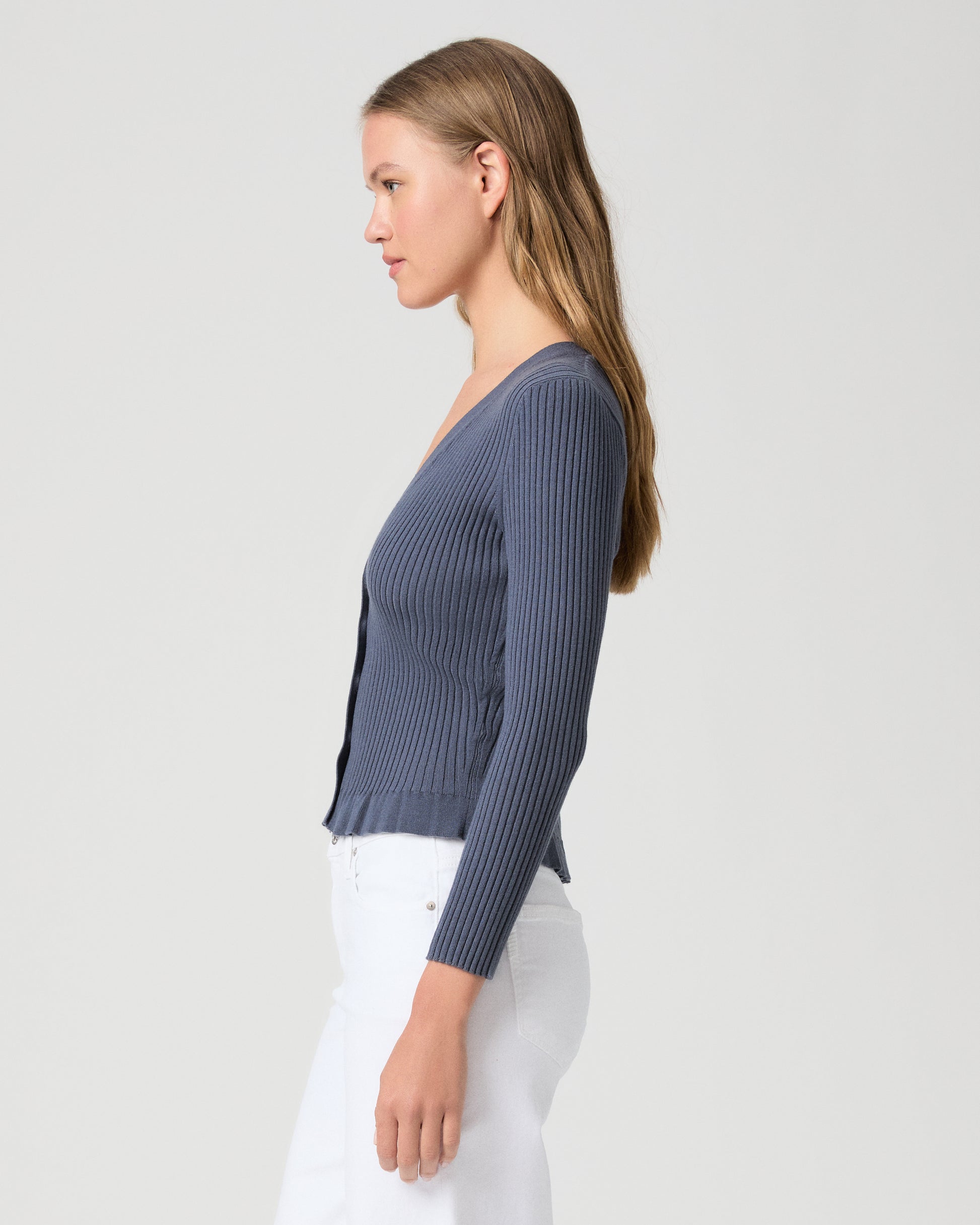 Woman wearing a blue ribbed cardigan and white pants on a light gray background