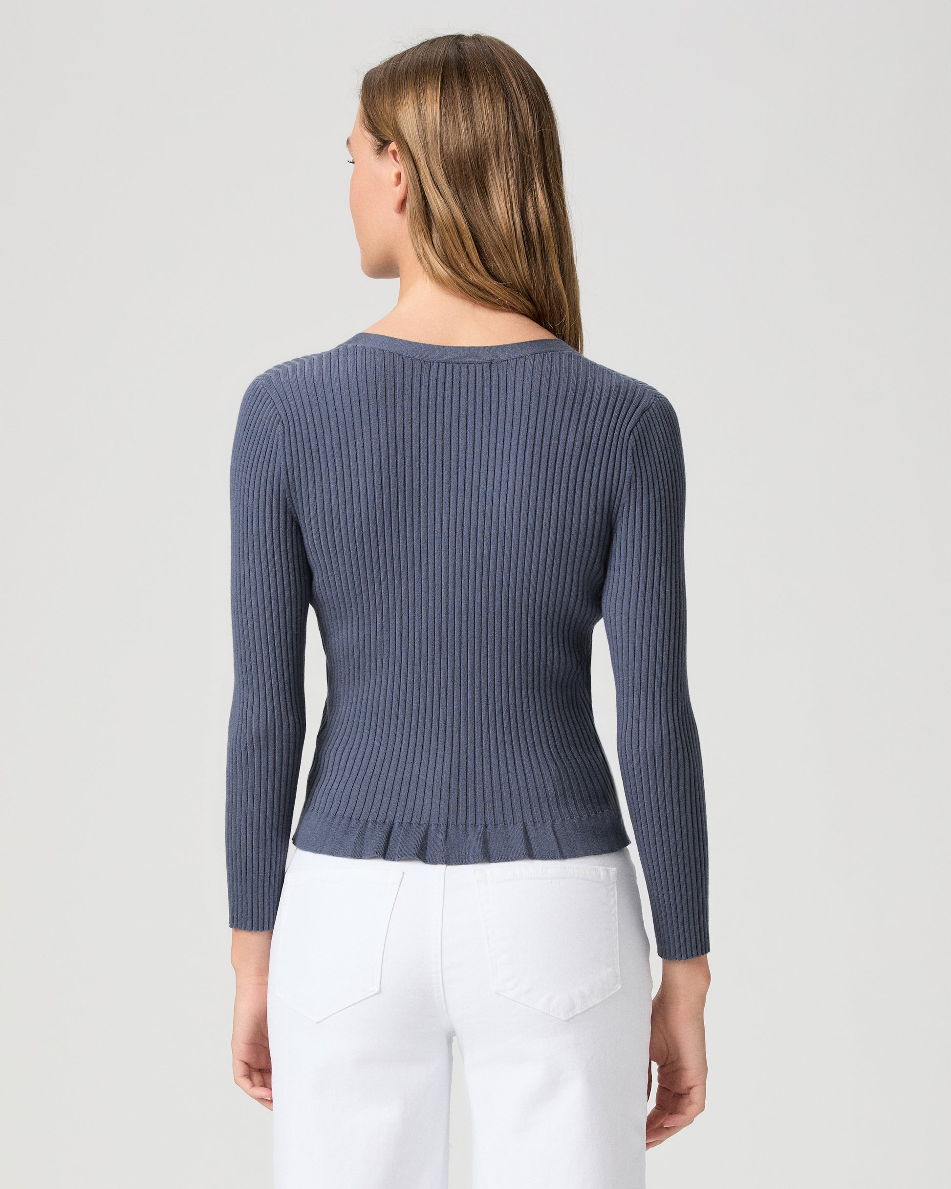 Woman wearing a blue ribbed cardigan and white pants on a light gray background