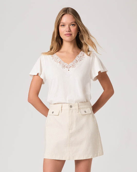 Woman wearing a white blouse with lace details and a cream-colored skirt on a plain background
