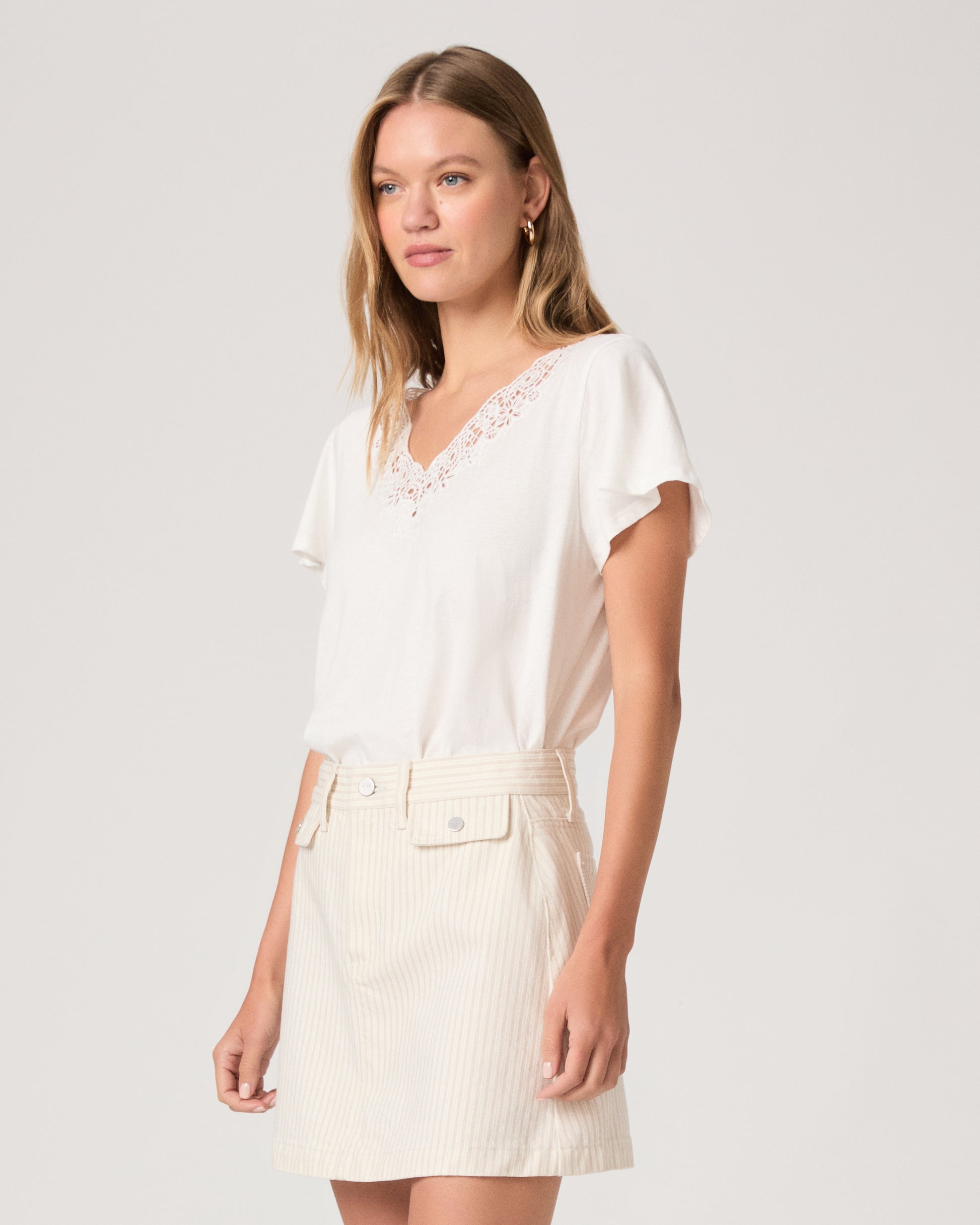 Woman wearing a white top paired with off white skirt on a white background