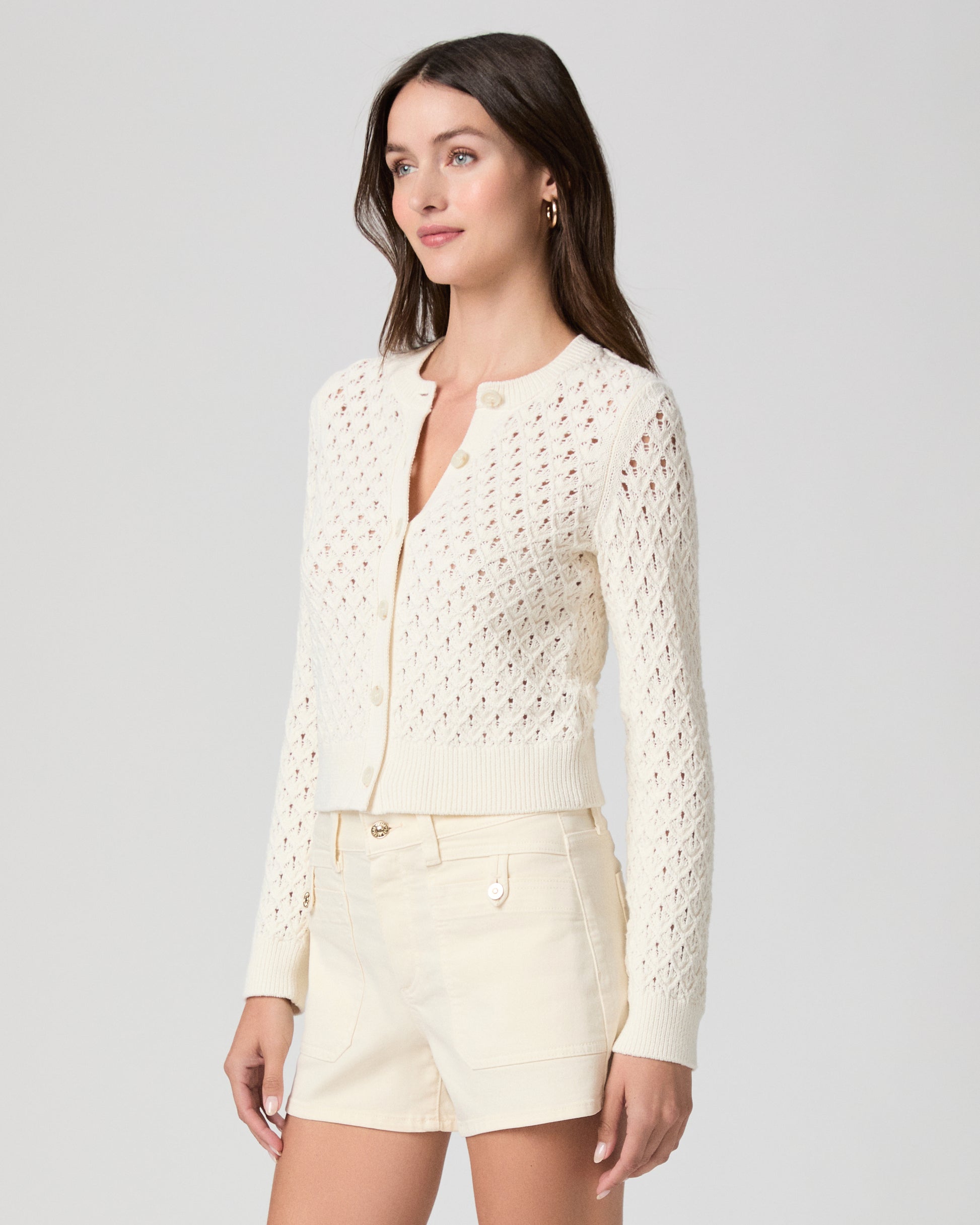Woman wearing a cream-colored lace top and shorts on a light gray background