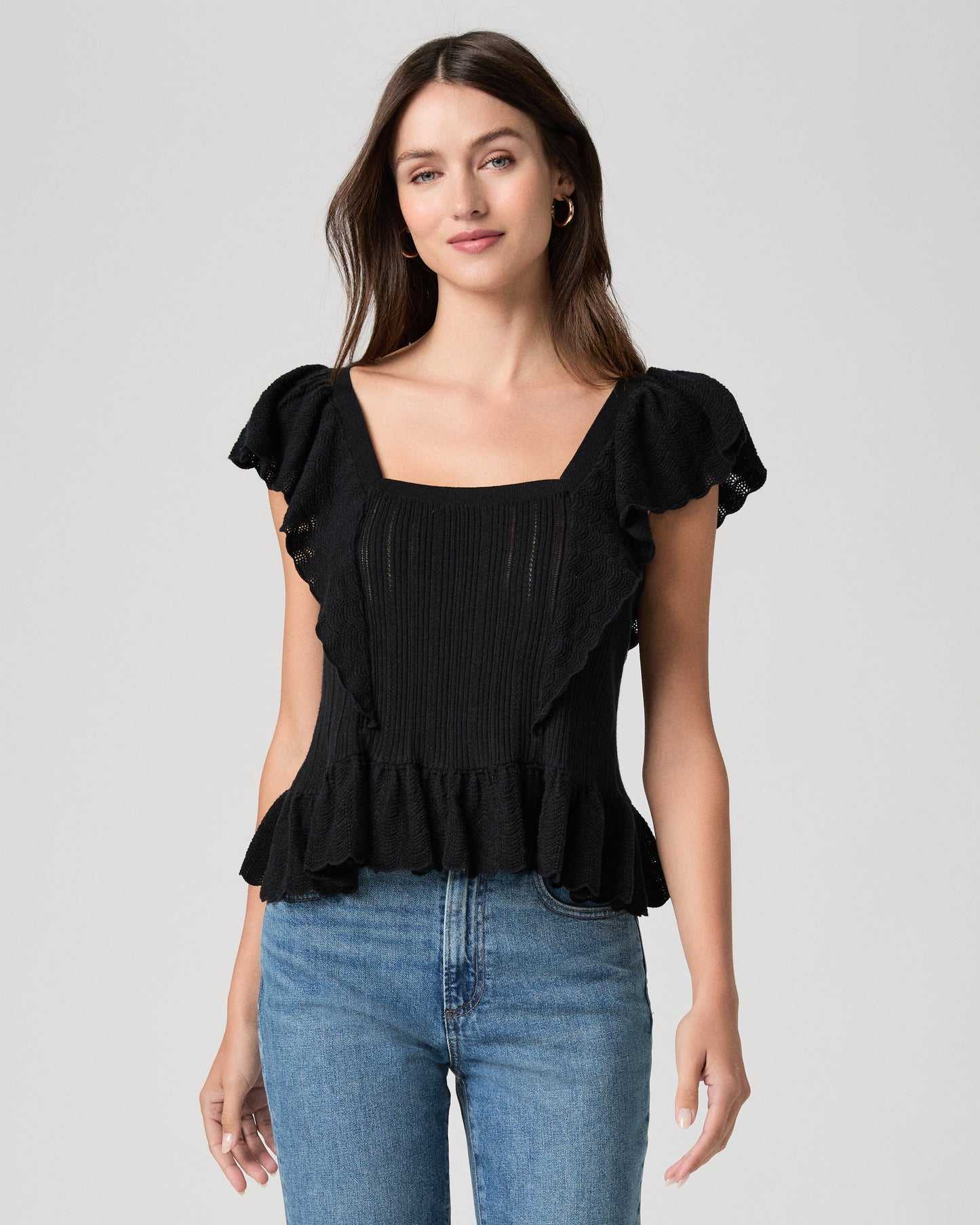 Woman wearing a black ruffled top and blue jeans on a gray background