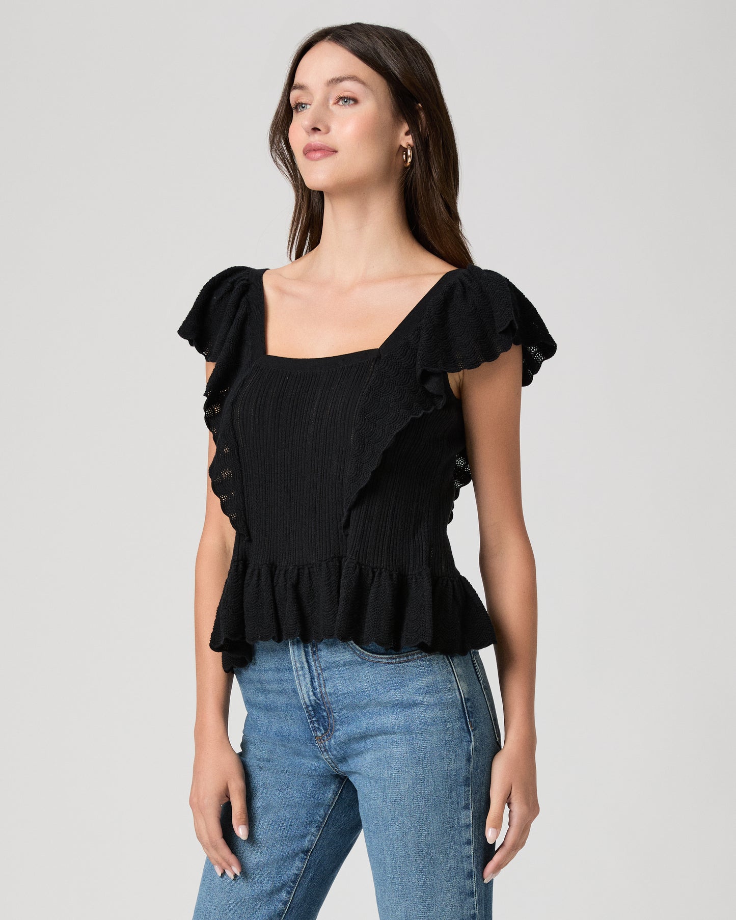 Woman wearing a black ruffled top and blue jeans on a gray background