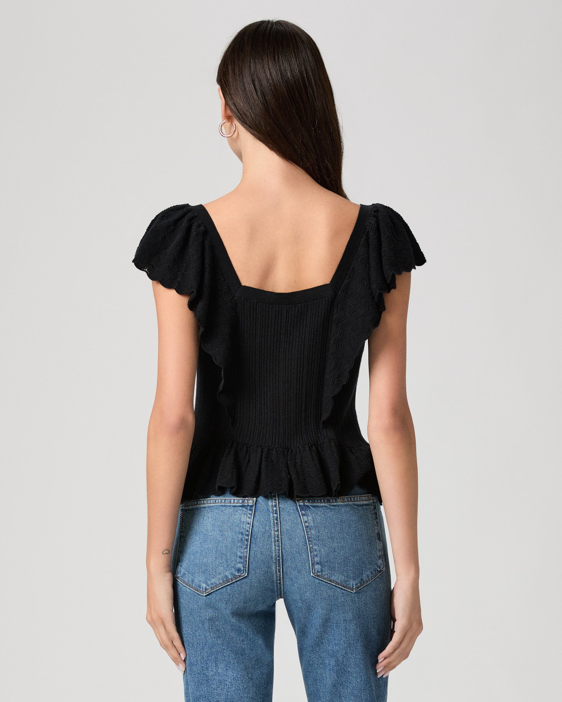 Woman wearing a black ruffled top and blue jeans on a gray background