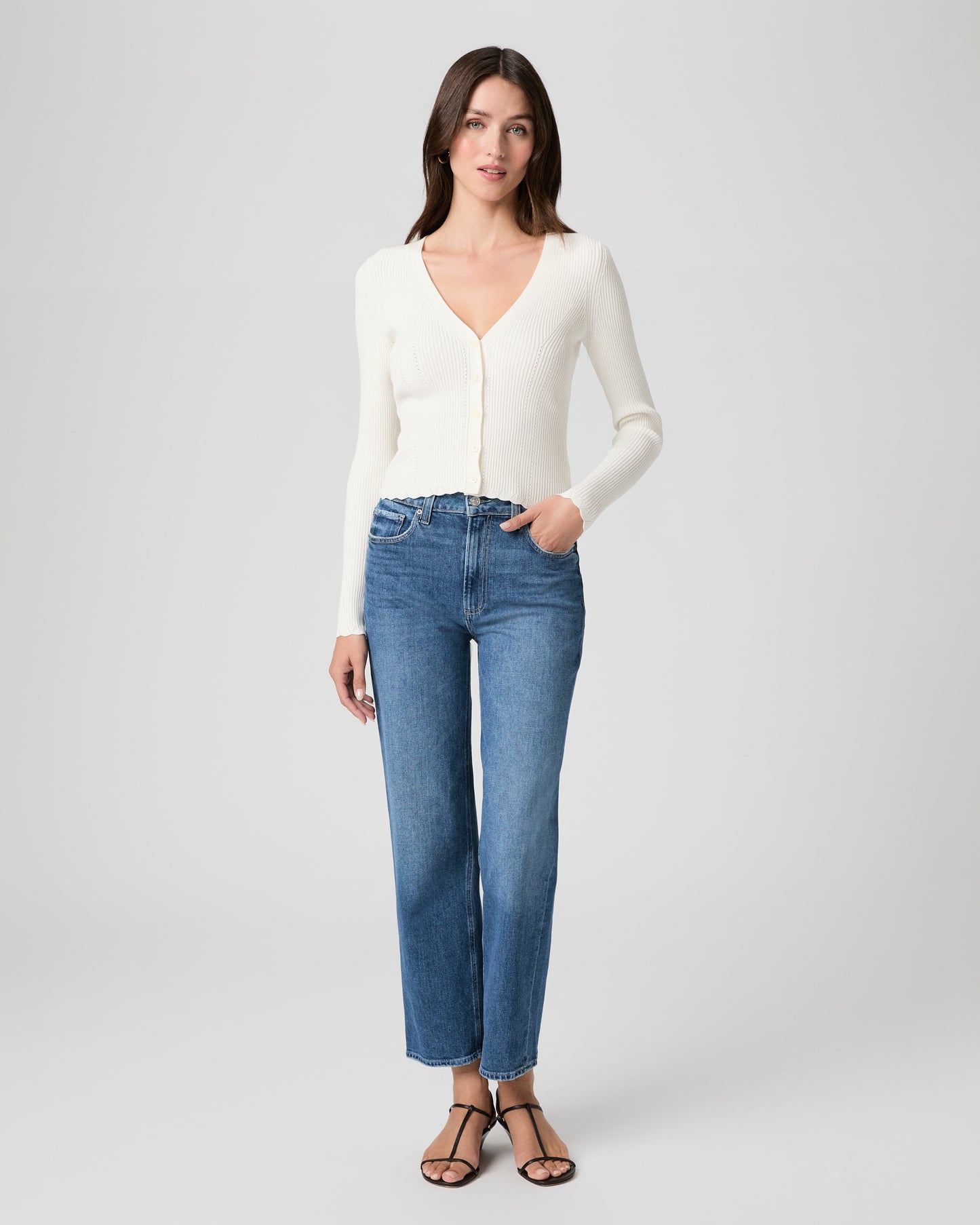 Woman wearing a white sweater and blue jeans on a plain background