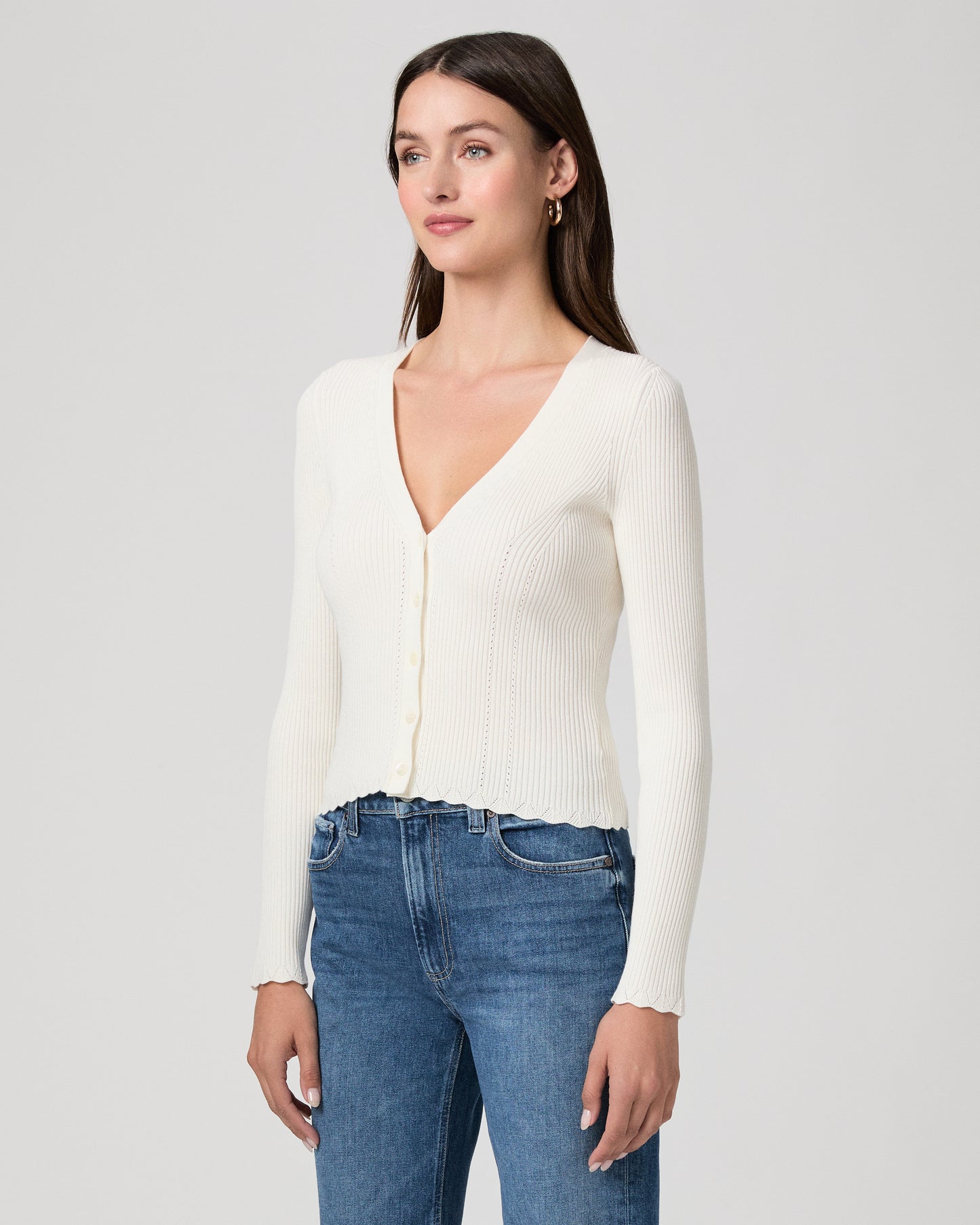 Woman wearing a white sweater and blue jeans on a plain background