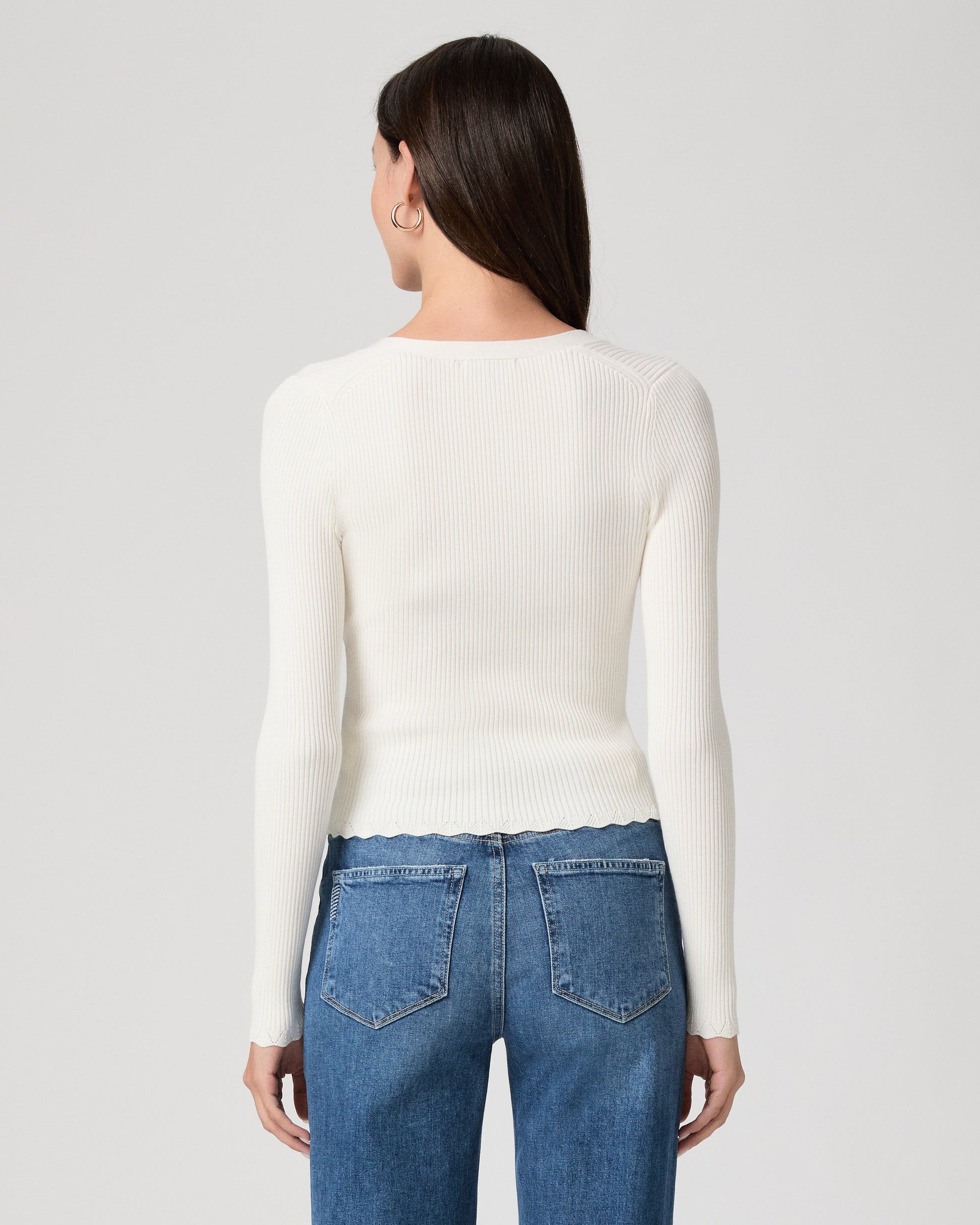 Woman wearing a white sweater and blue jeans on a plain background