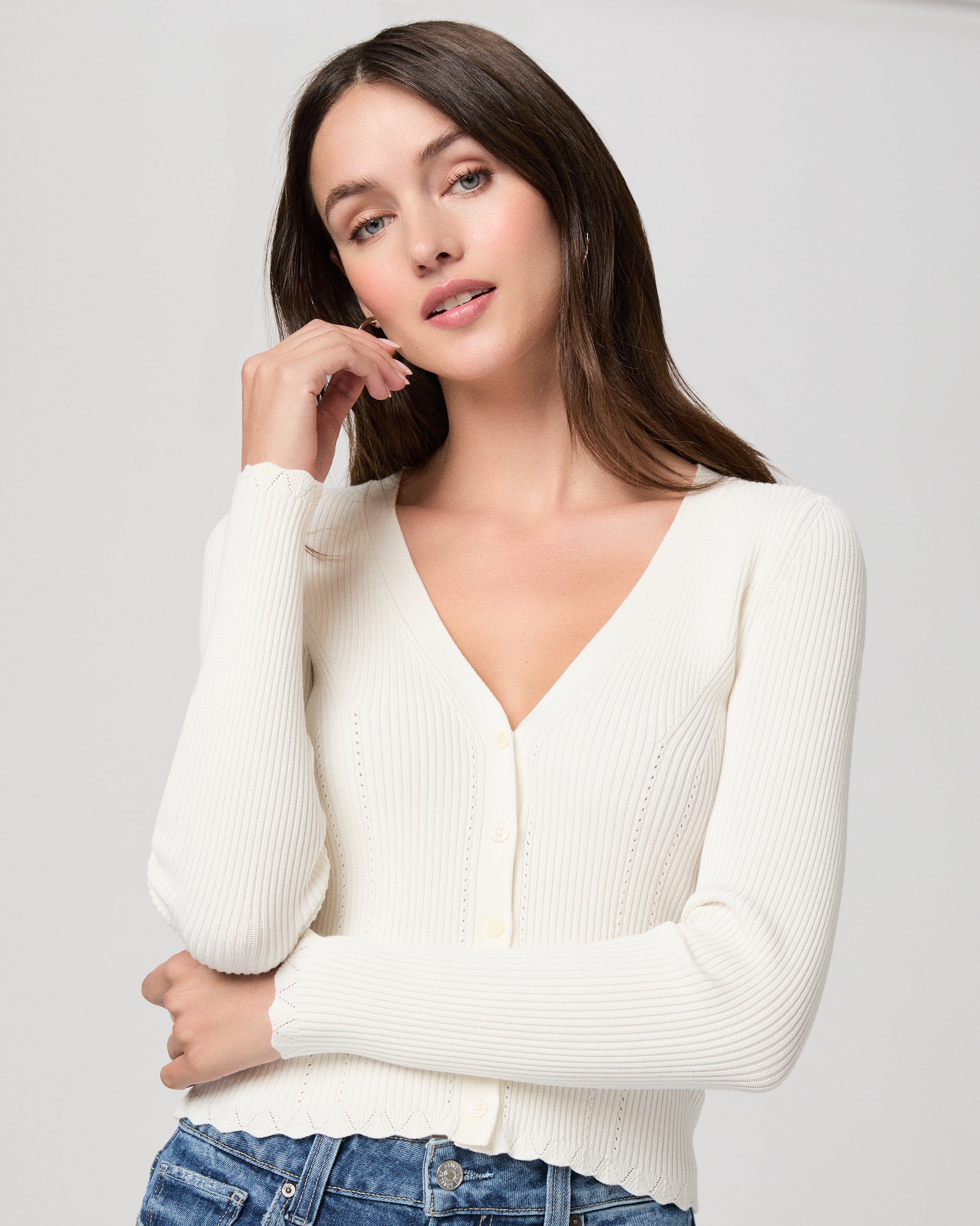 Woman wearing a white sweater and blue jeans on a plain background