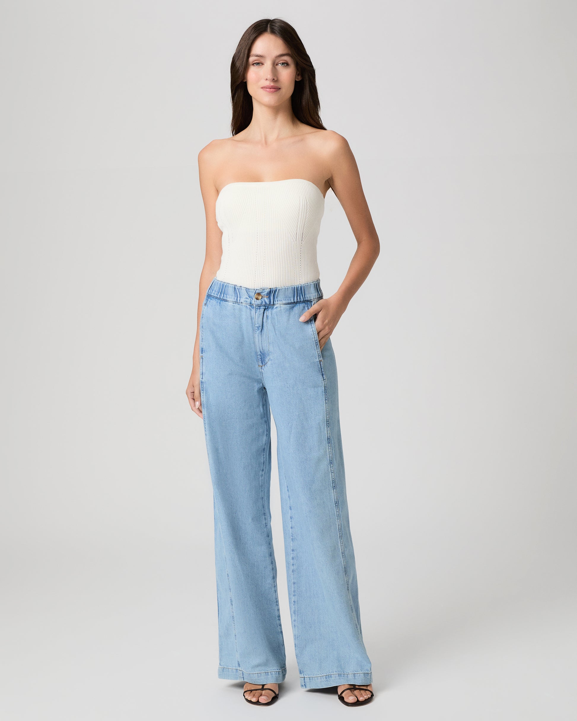Woman wearing a white strapless top and blue jeans against a plain background