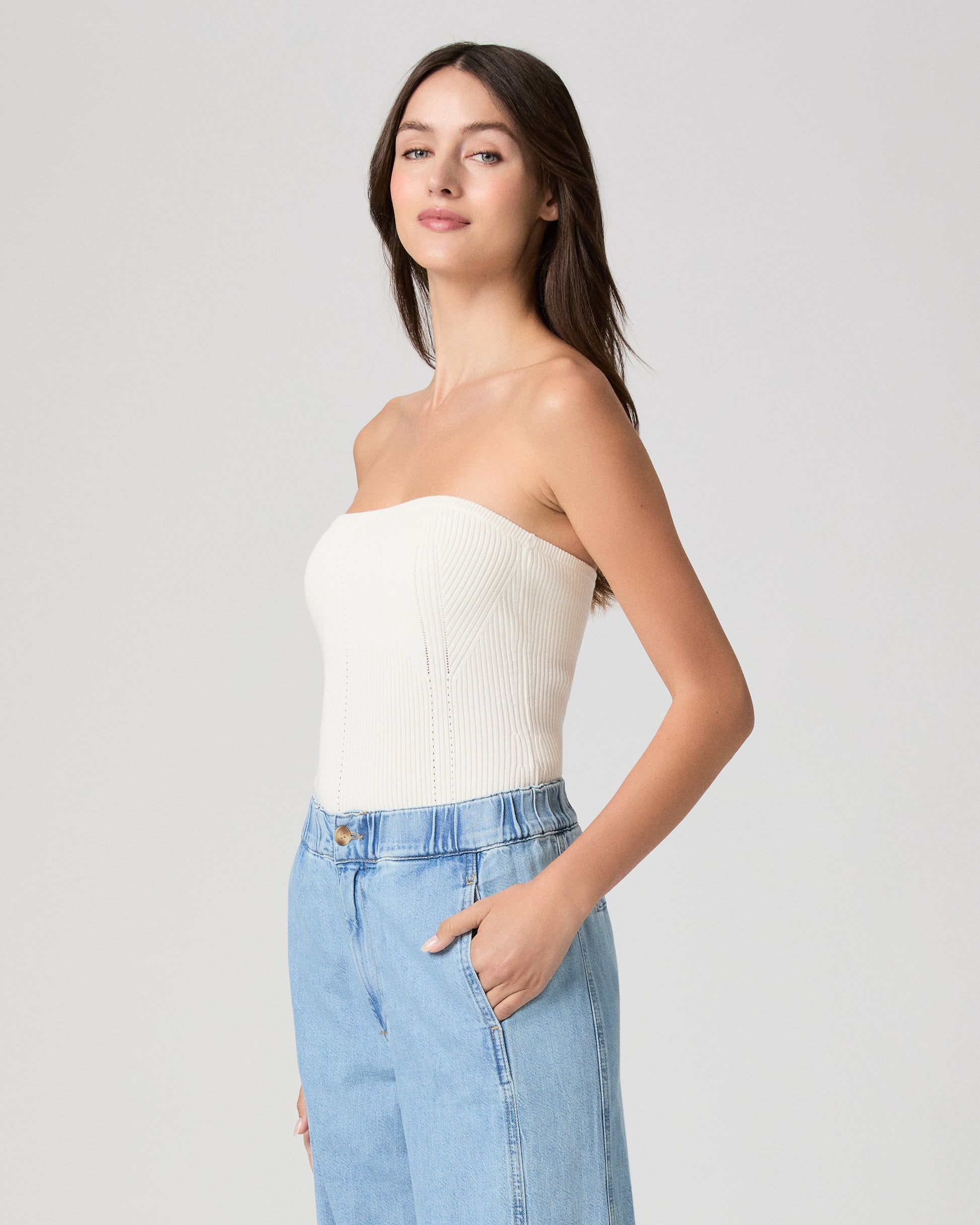 Woman wearing a white strapless top and blue jeans against a plain background