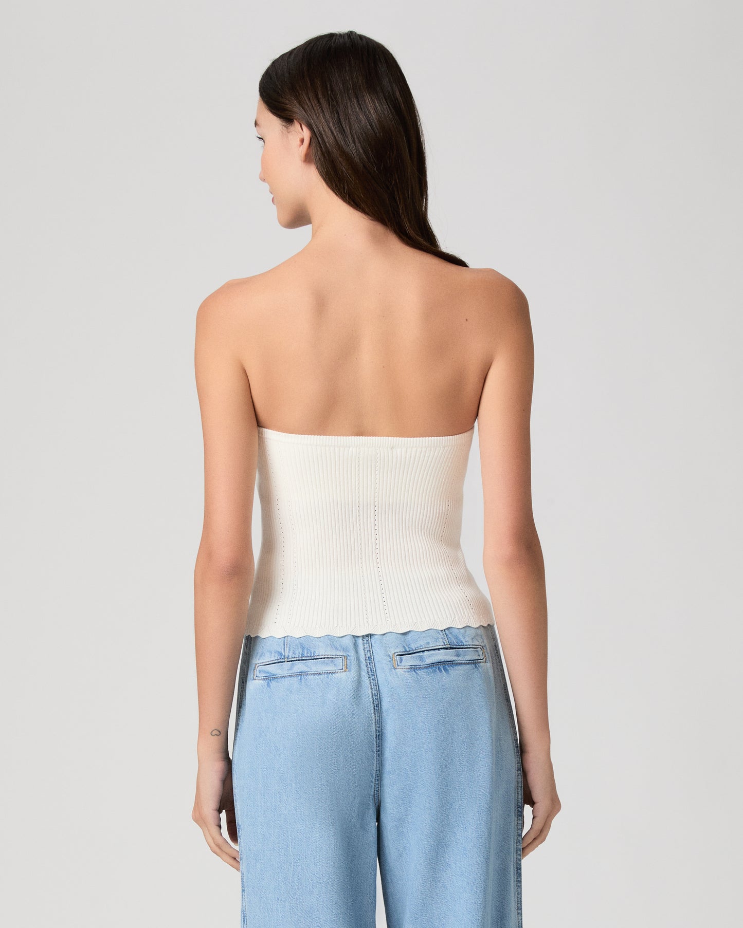 Woman wearing a white strapless top and blue jeans against a plain background