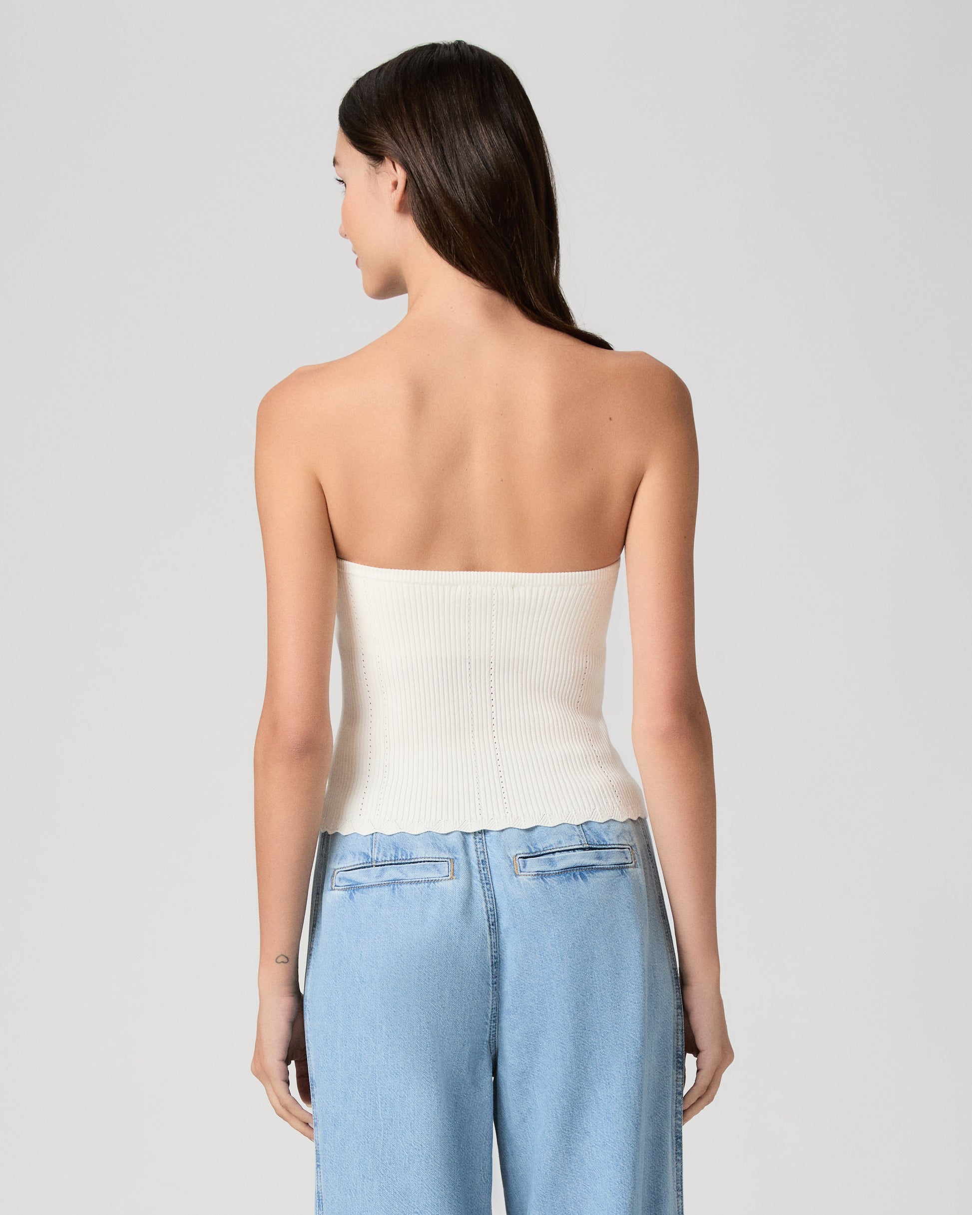 Woman wearing a white strapless top and blue jeans against a plain background