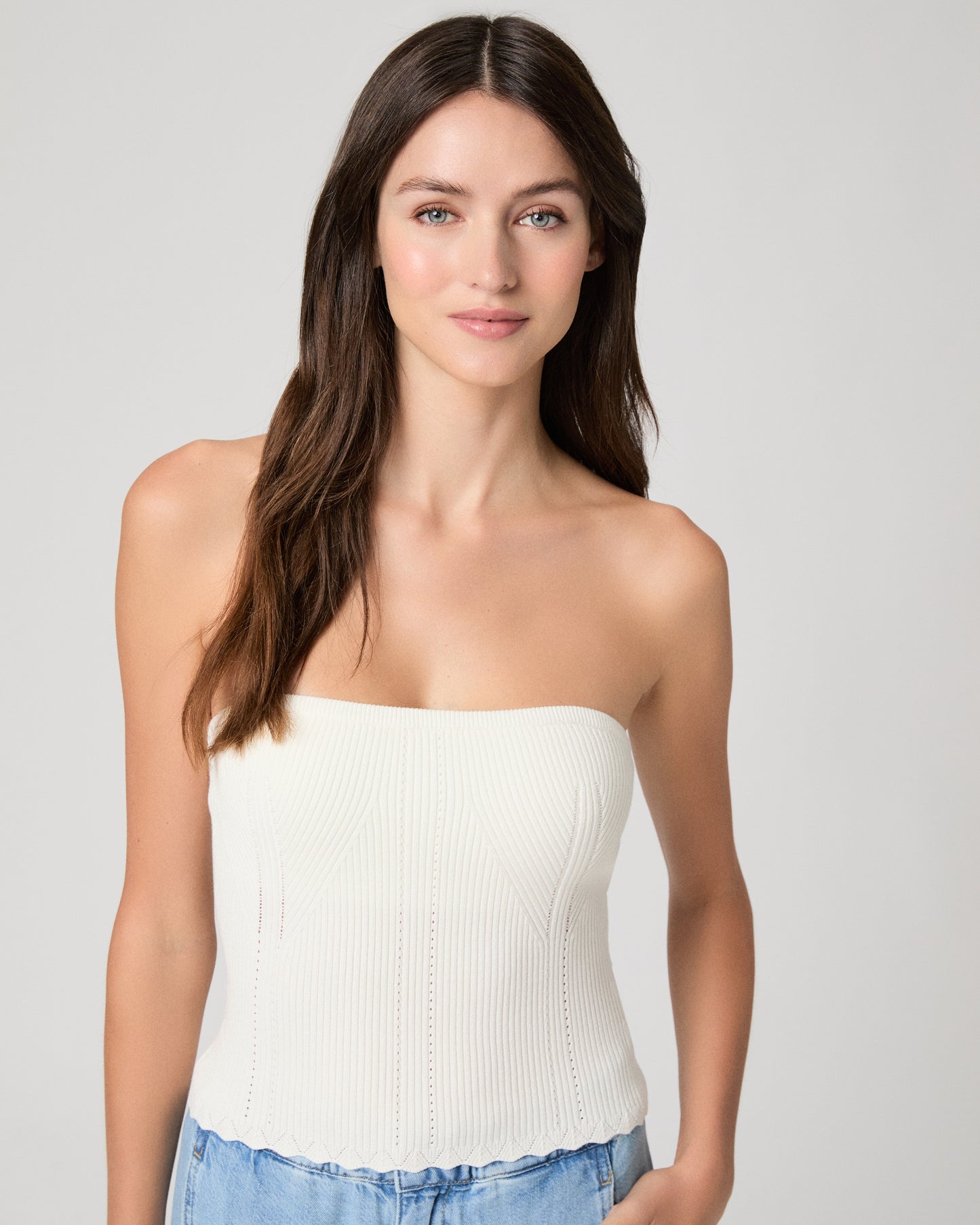 Woman wearing a white strapless top and blue jeans against a plain background