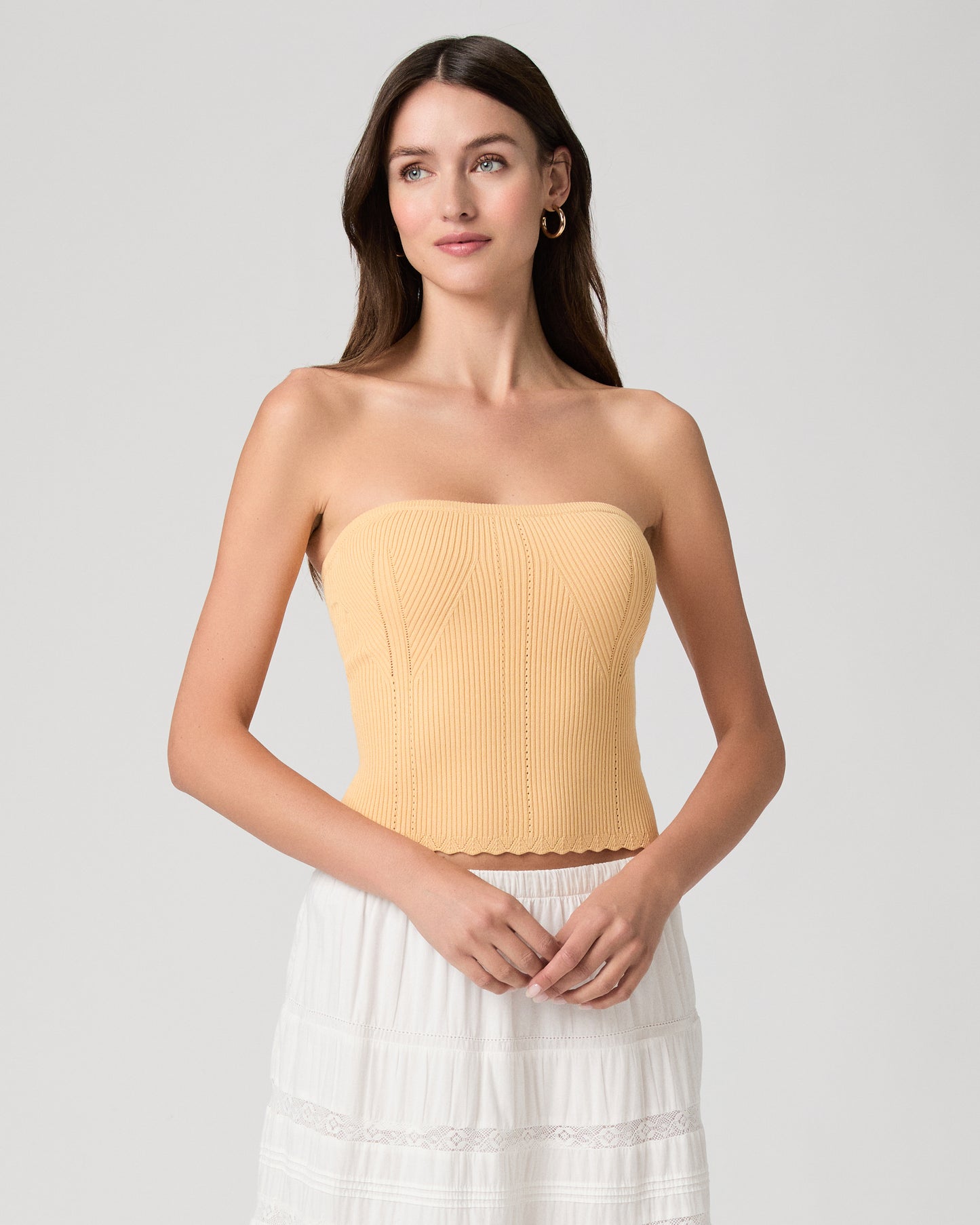 Woman wearing a yellow strapless top and white skirt on a light gray background
