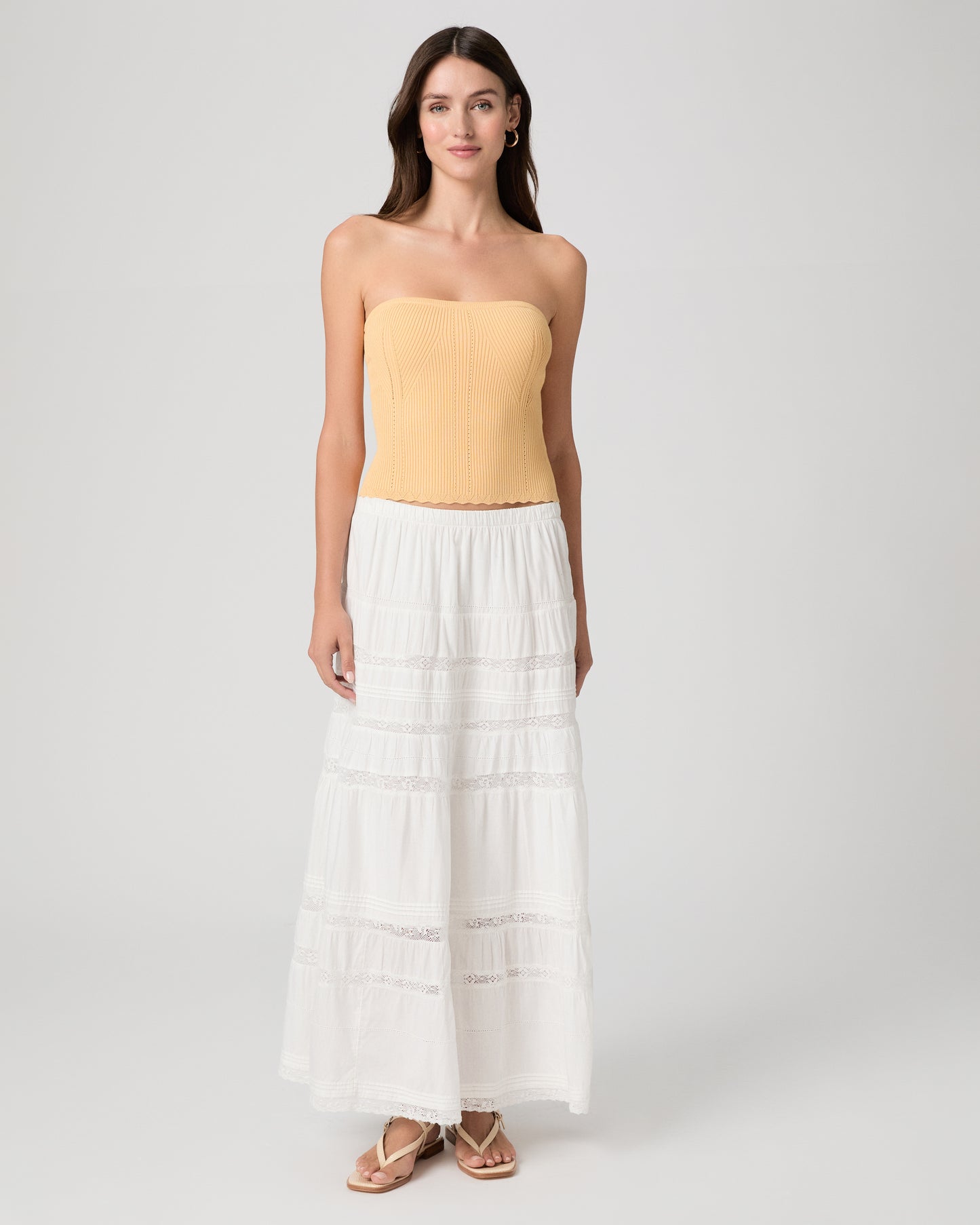 Woman wearing a yellow strapless top and white skirt on a light gray background