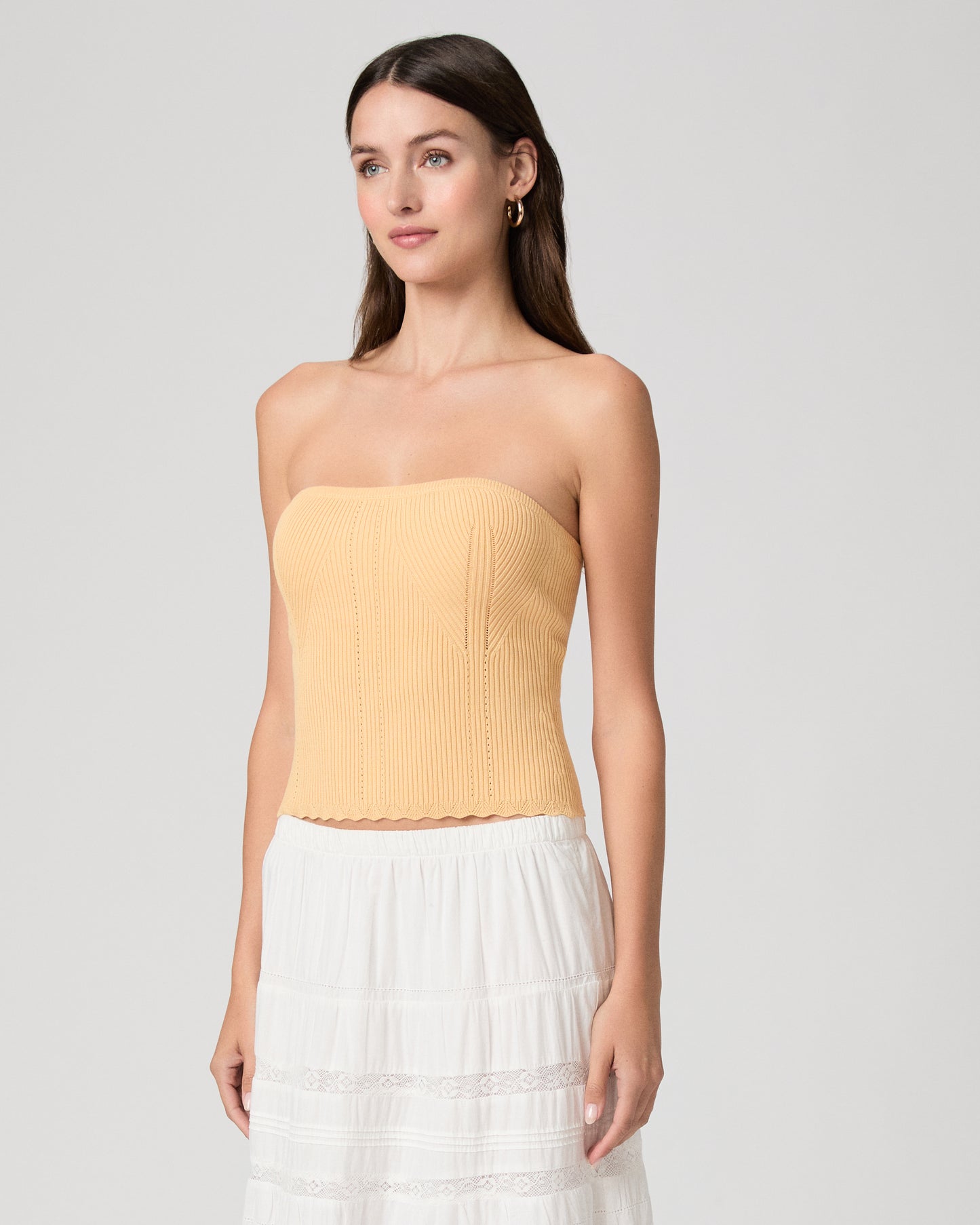 Woman wearing a yellow strapless top and white skirt on a light gray background