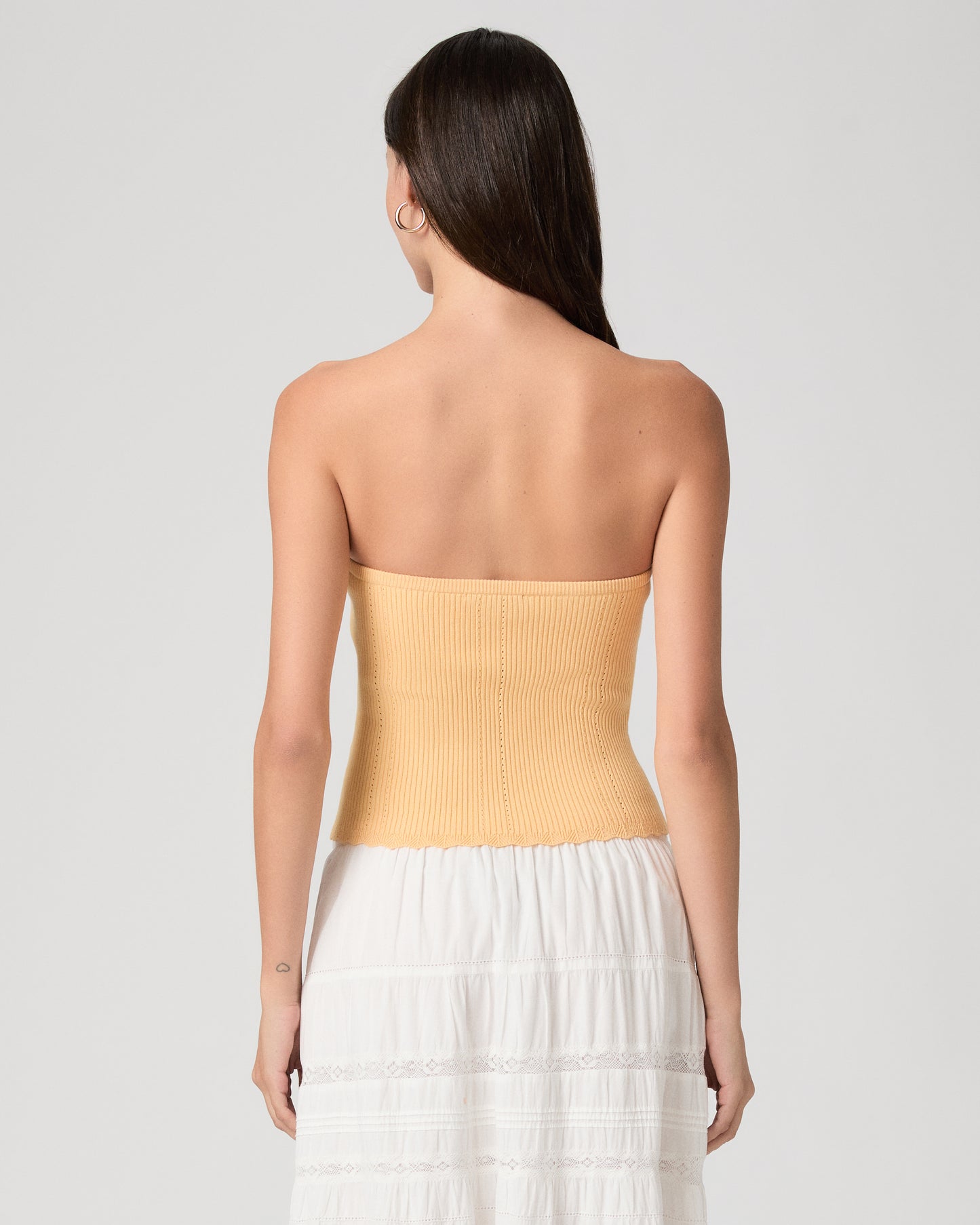 Woman wearing a yellow strapless top and white skirt on a light gray background