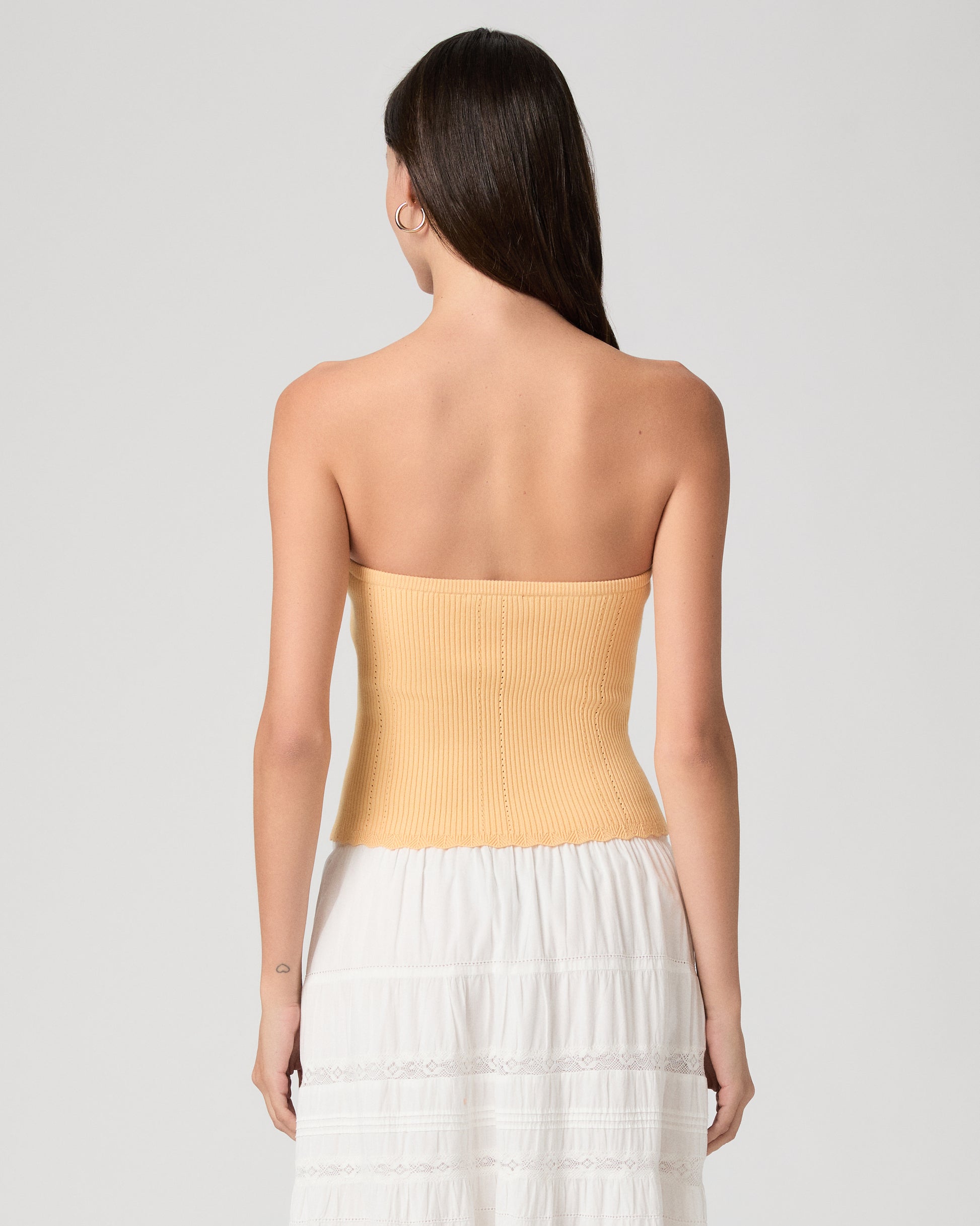 Woman wearing a yellow strapless top and white skirt on a light gray background
