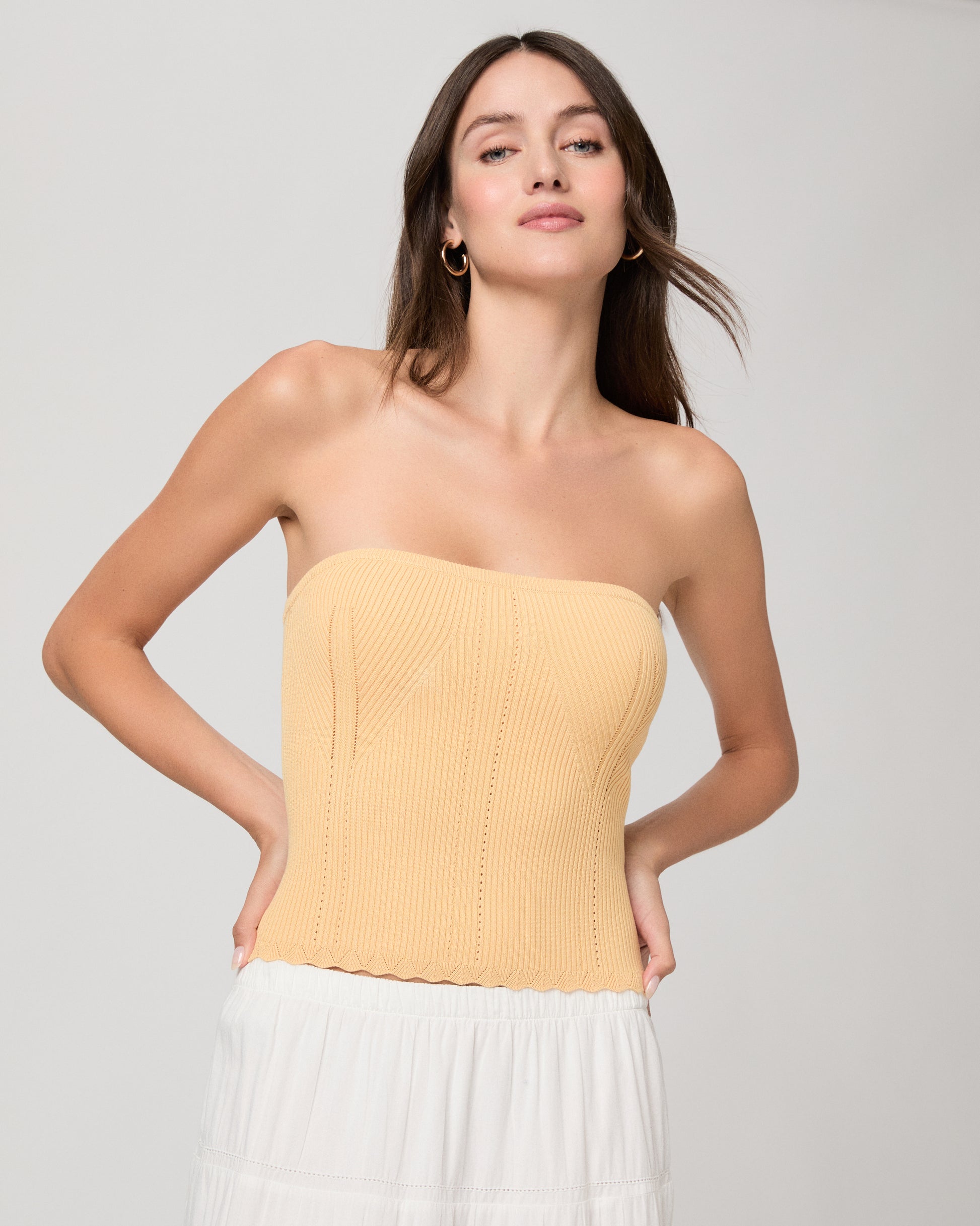 Woman wearing a yellow strapless top and white skirt on a light gray background